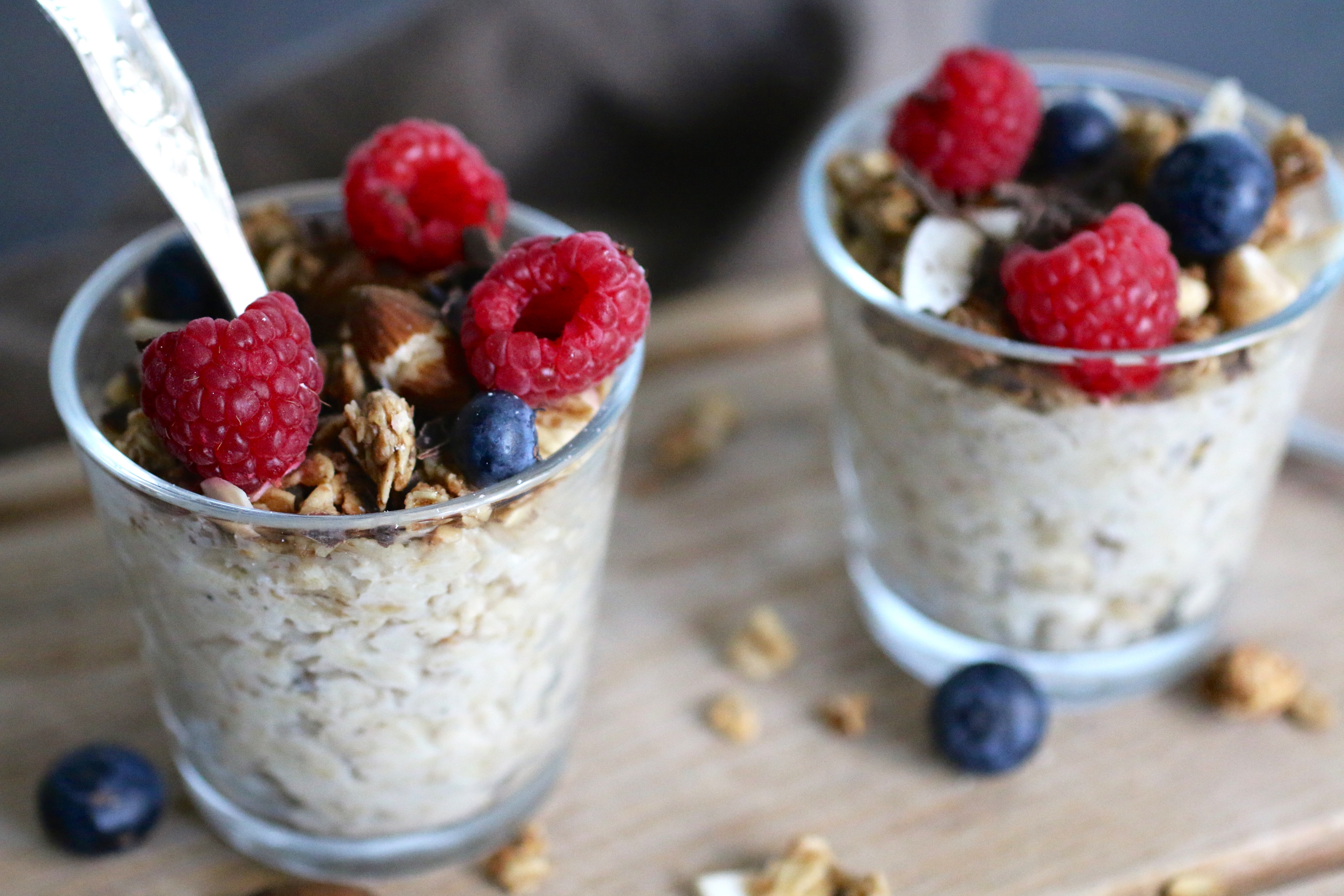 Två glas med overnight oats toppade med hallon och blåbär.