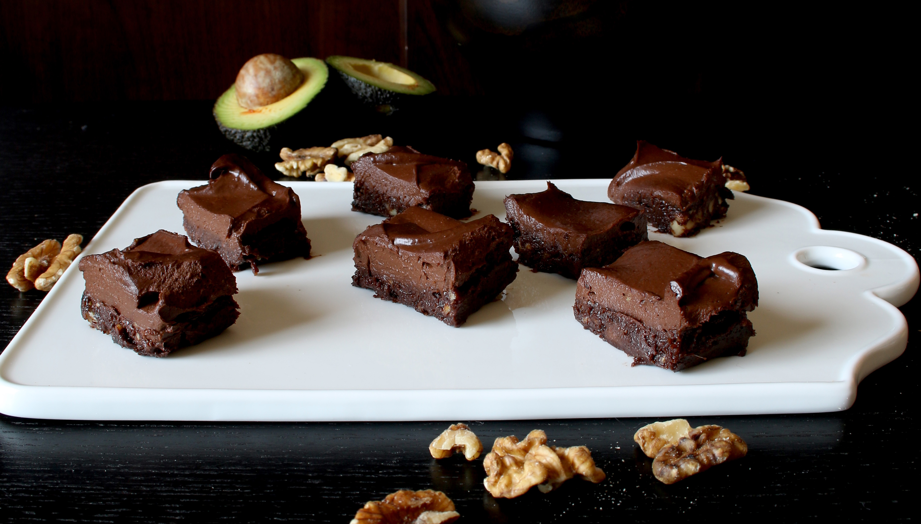 Raw brownie i bitar på en vit skärbräda.