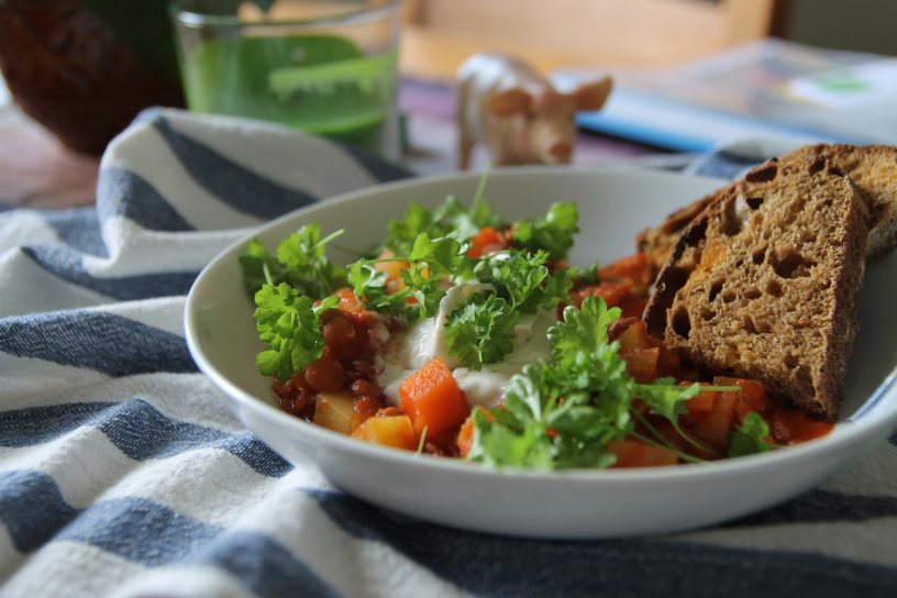 Linsgulasch med persilja i en vit skål står på ett bord med rutig duk