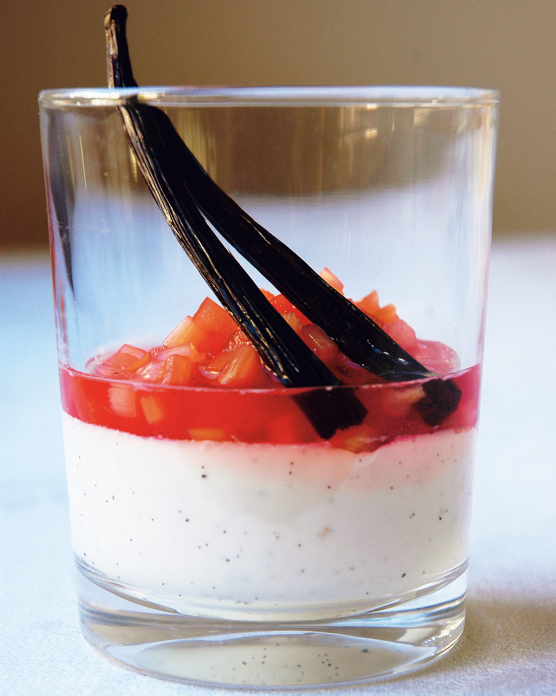 Pannacotta med kokosmjölk och rabarberkompott i ett glas, dekorerad med vaniljstång.