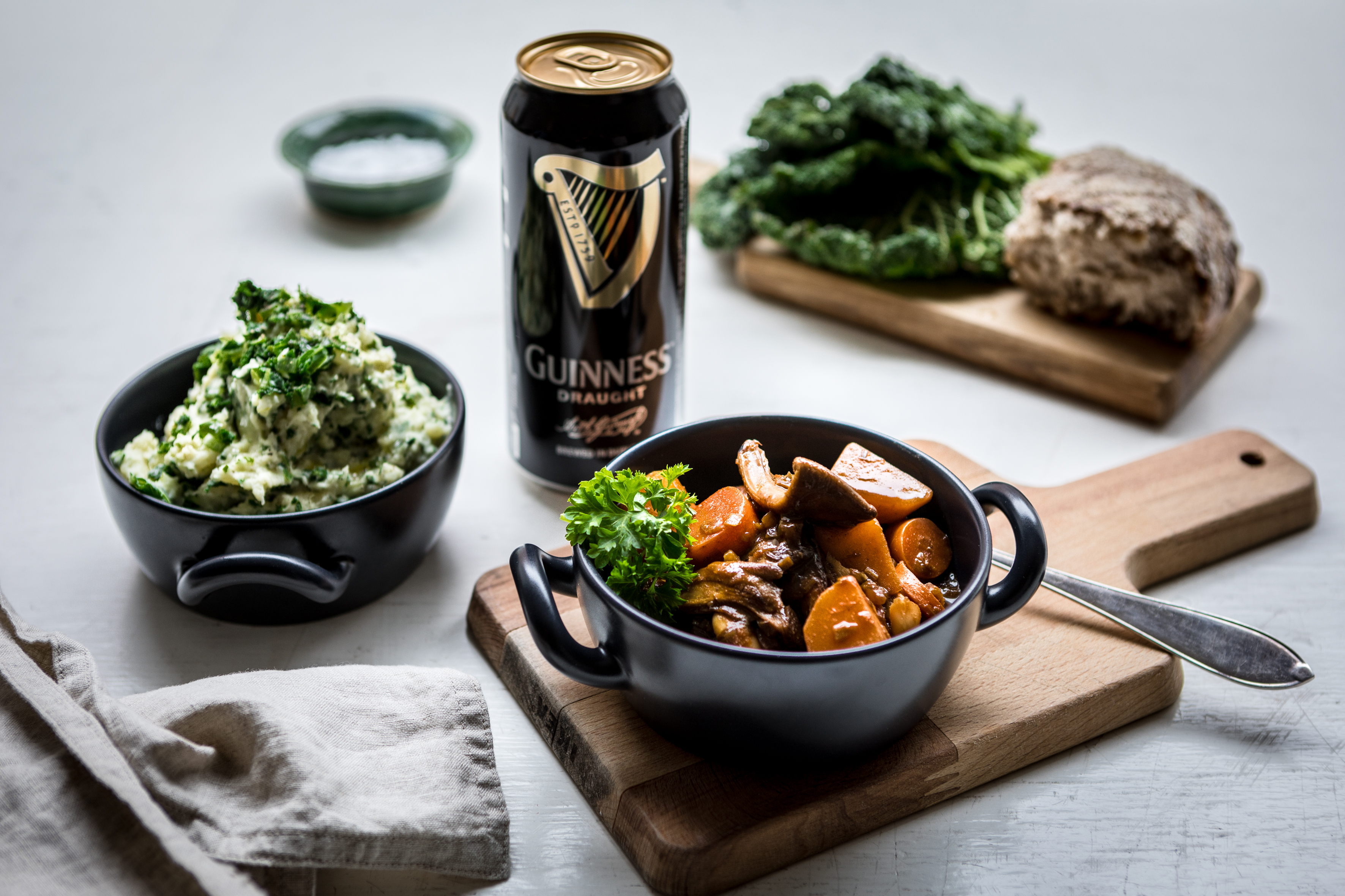 En skål med Irish stew står på en skärbräda bredvid en skål med irländskt potatismos och en öl