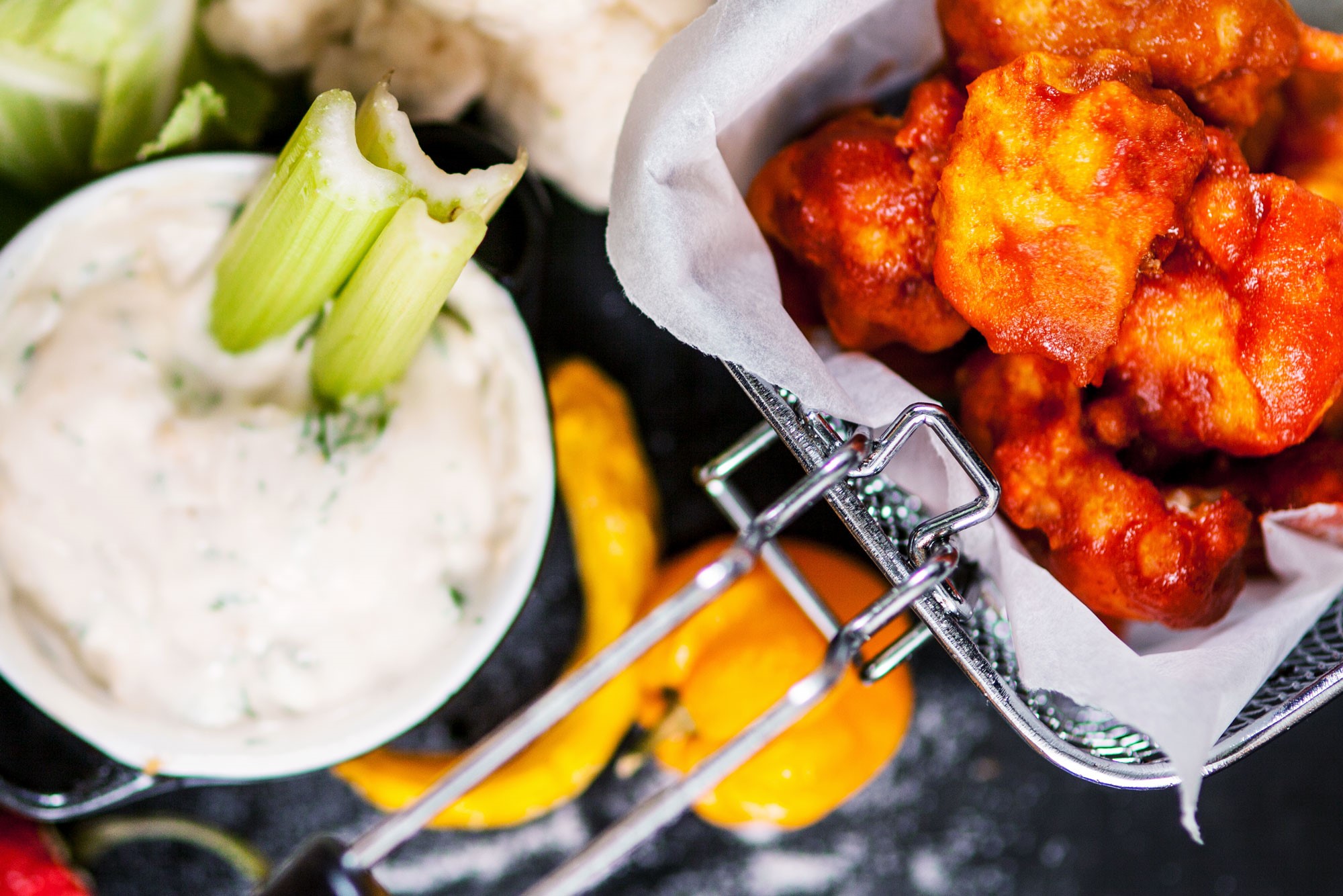 Buffalo wings av blomkål i en frityrkorg, bredvid står en skål med blåmögelostsås
