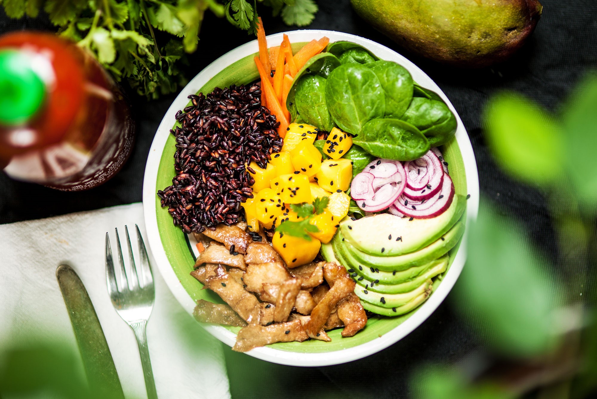 En pokébowl med babyspenat, mangobitar, vegobitar, svart ris och avokado.