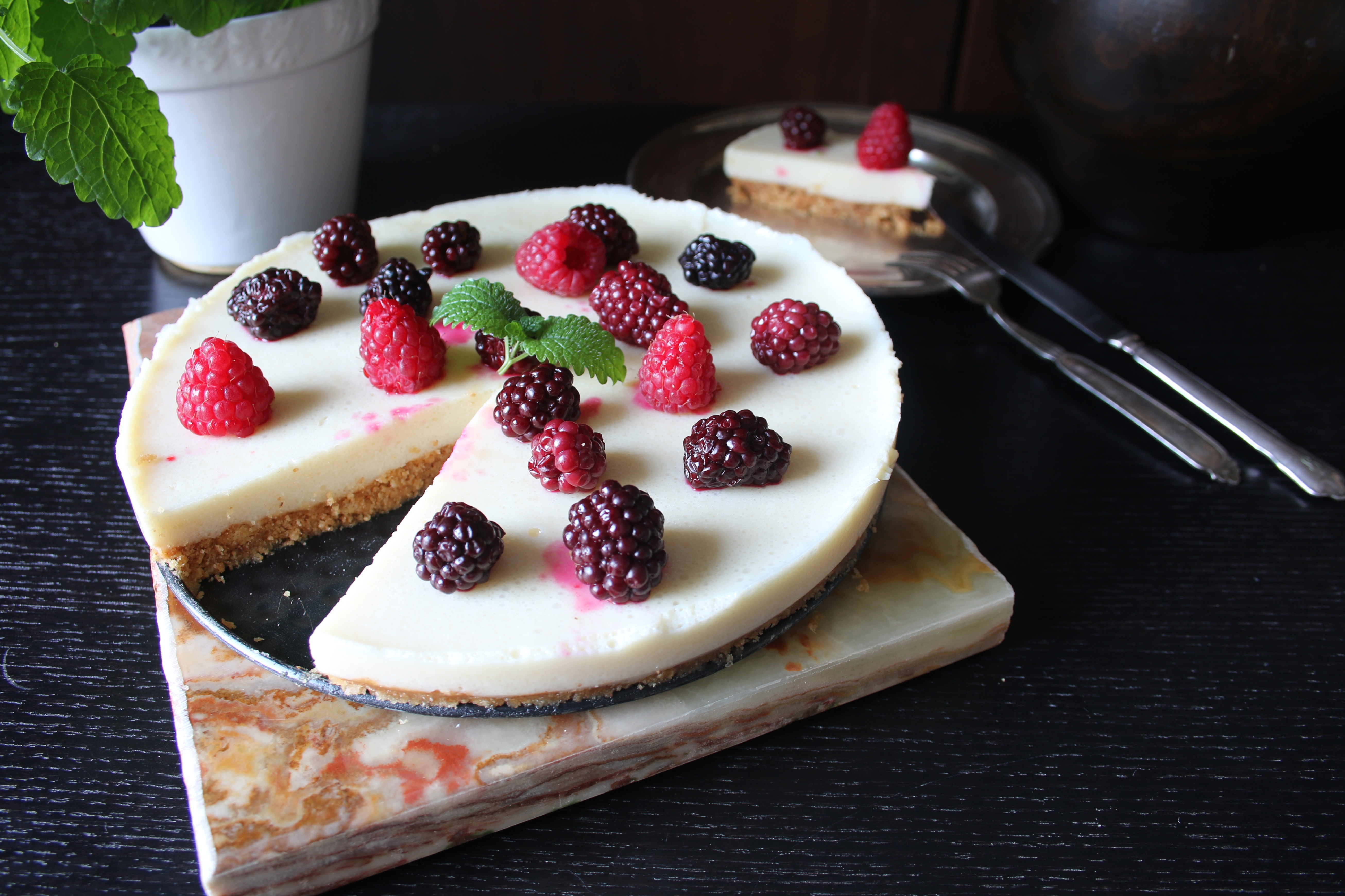 Cheesecake med citronfyllning dekorerad med hallon och björnbär på ett mörkt bord