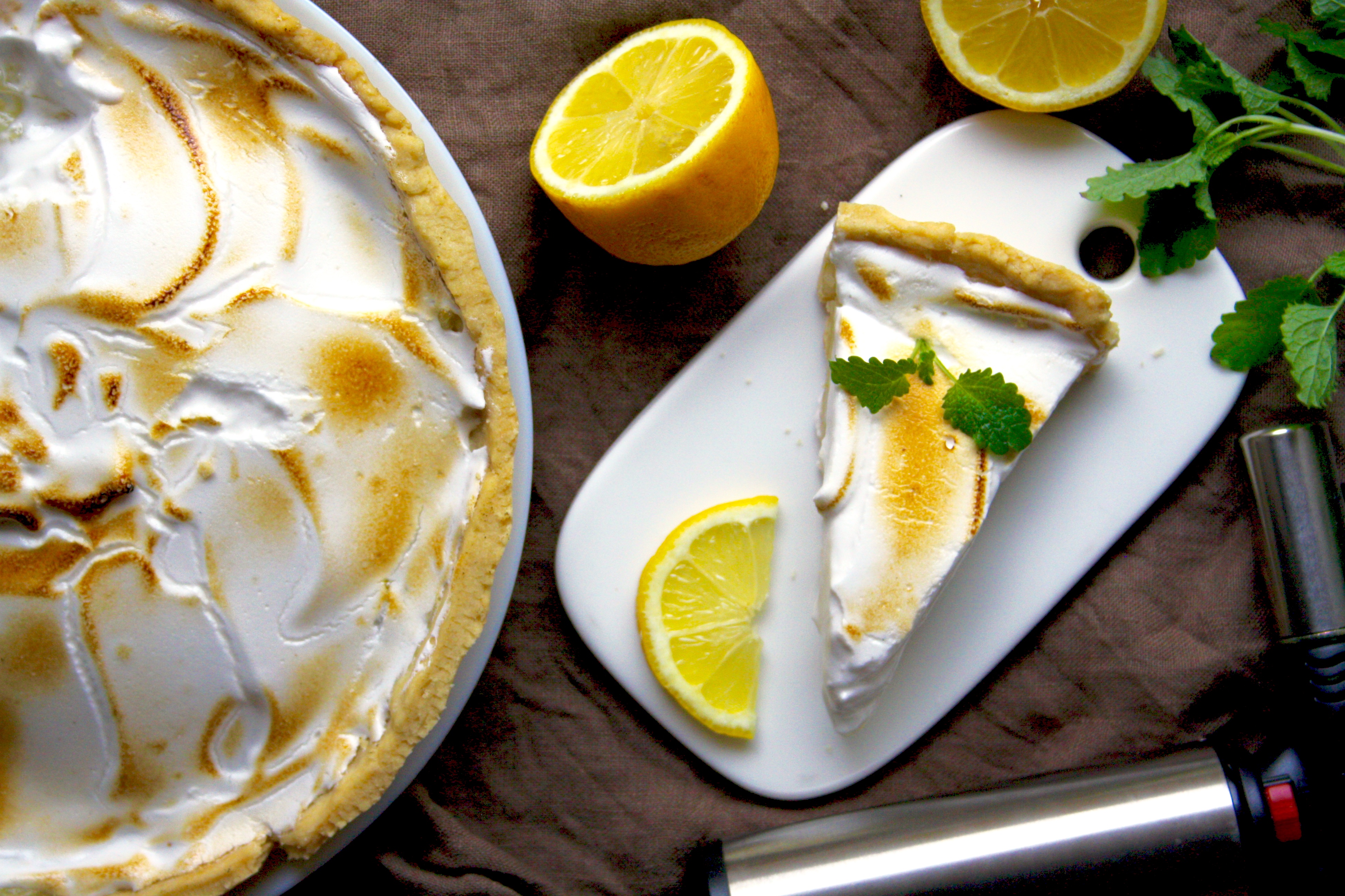 En citronpaj med marängtäcke, bredvid pajen ligger några delade citroner