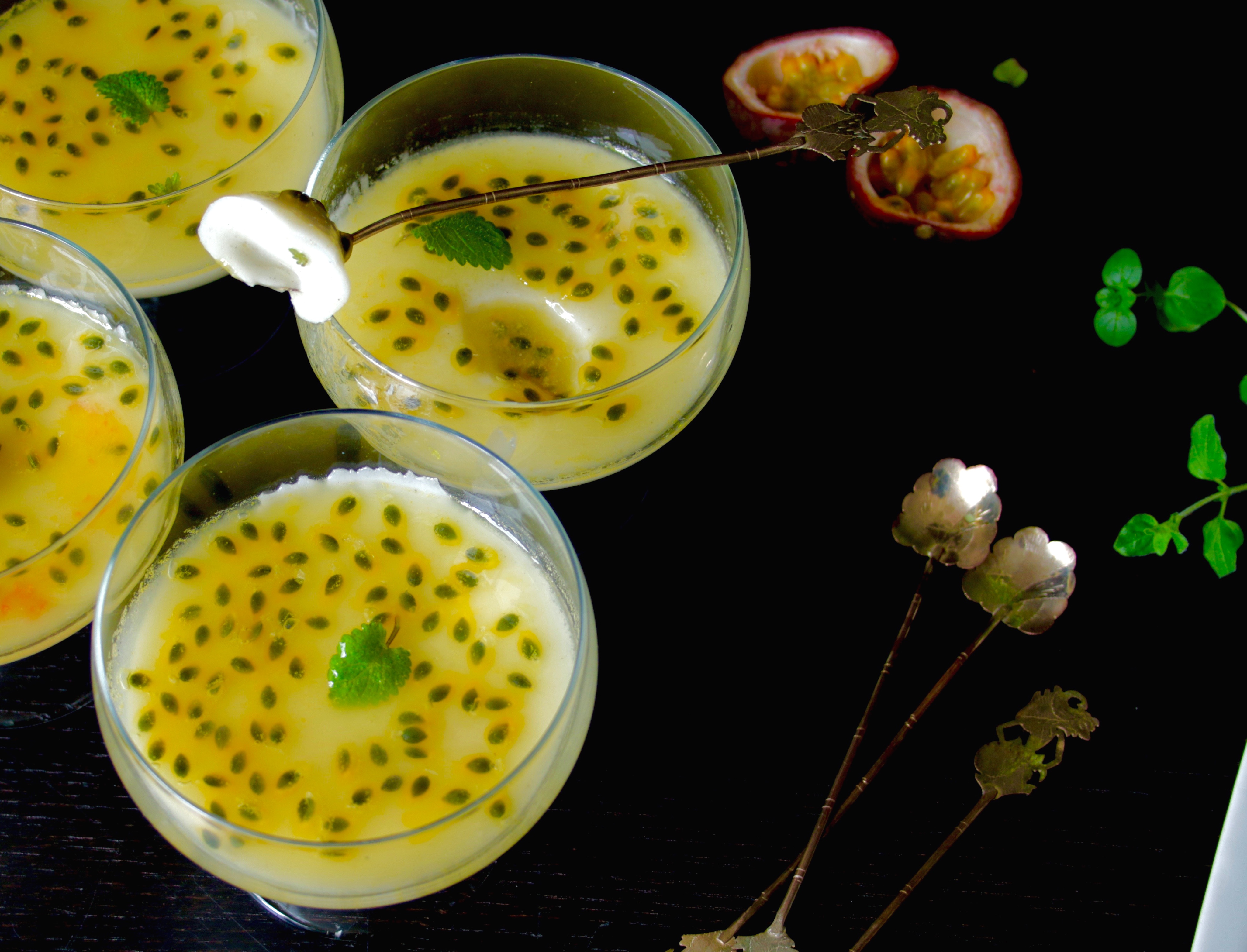 Fyra bägare med pannacotta med passionsfrukt på ett mörkt bord.