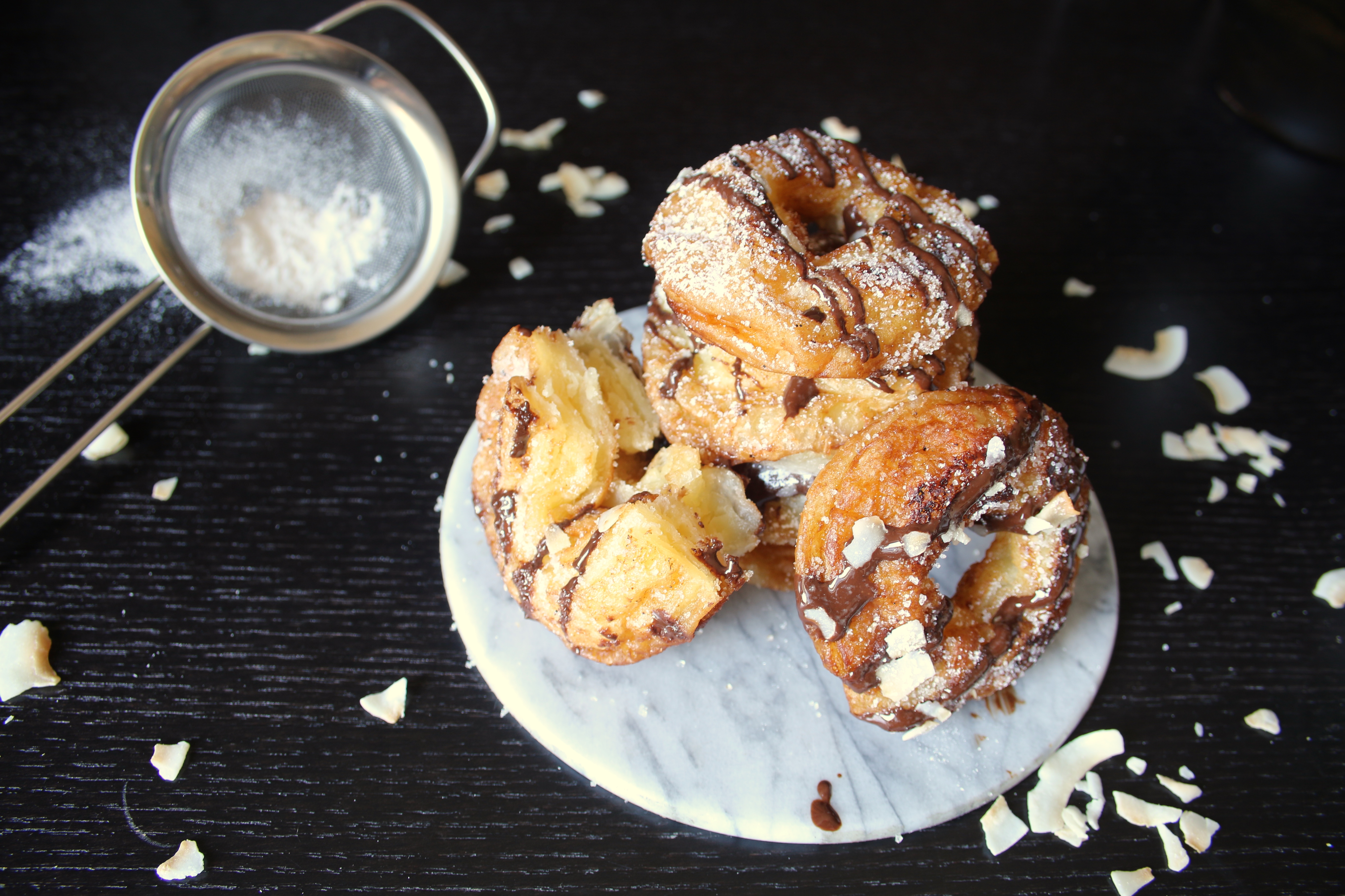 Cronuts med choklad och kokosflarn på ett vitt fat på ett mörkt bord