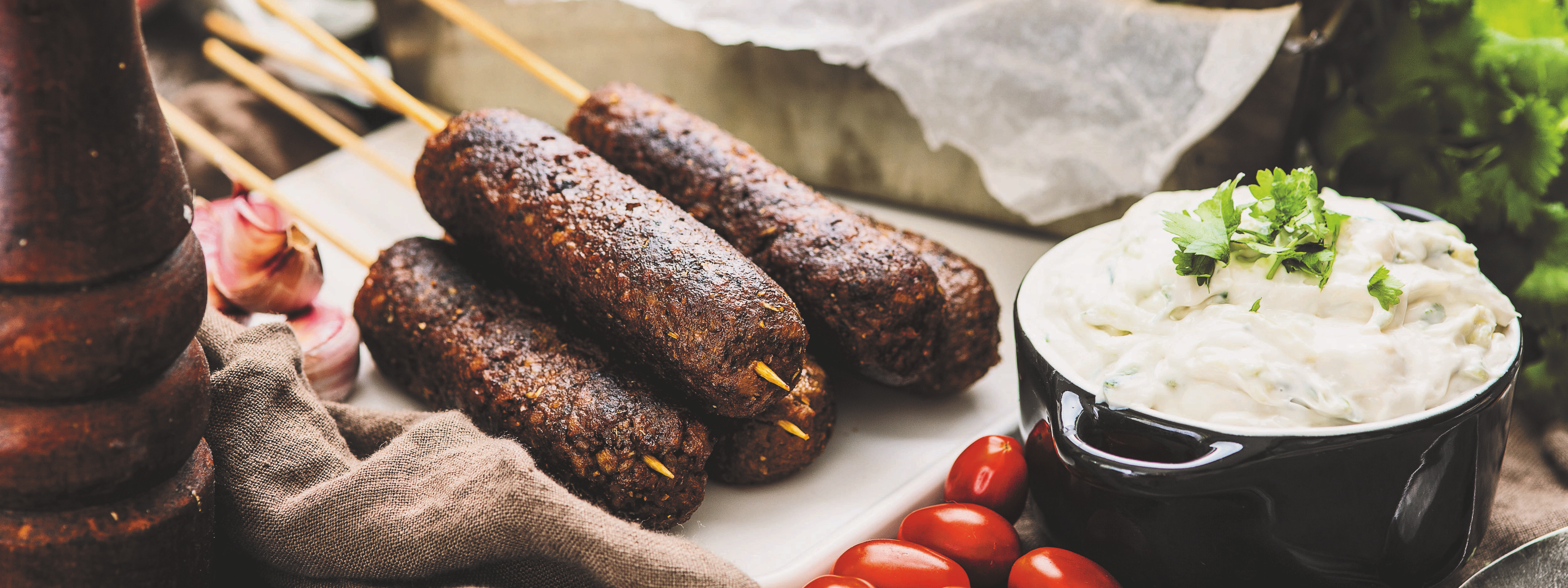 kebabspett på en vit skärbräda, bredvid spetten står en skål med tzatziki