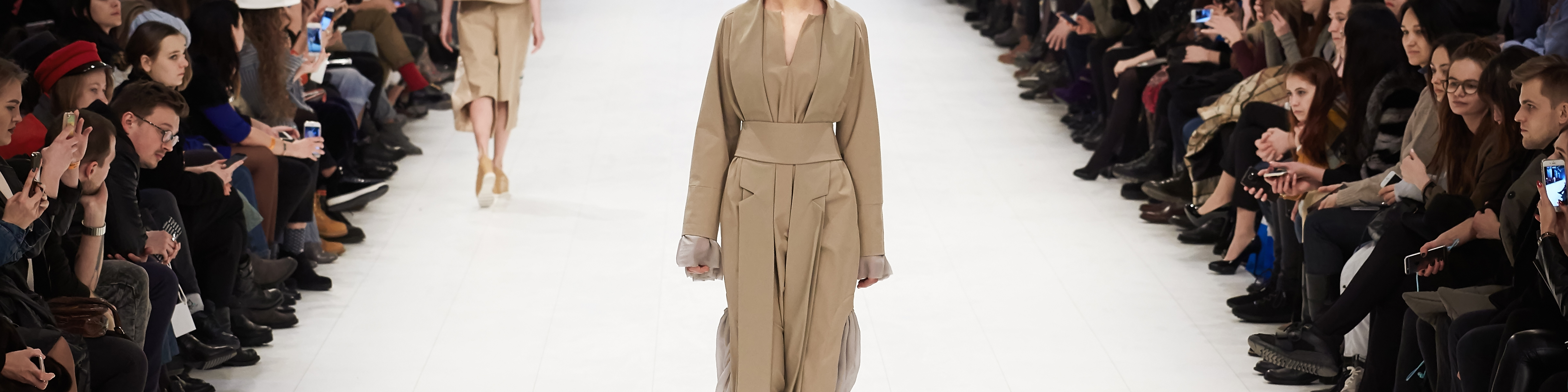 En catwalk med en person i mitten med en trenchcoat och åskådare på varje sida