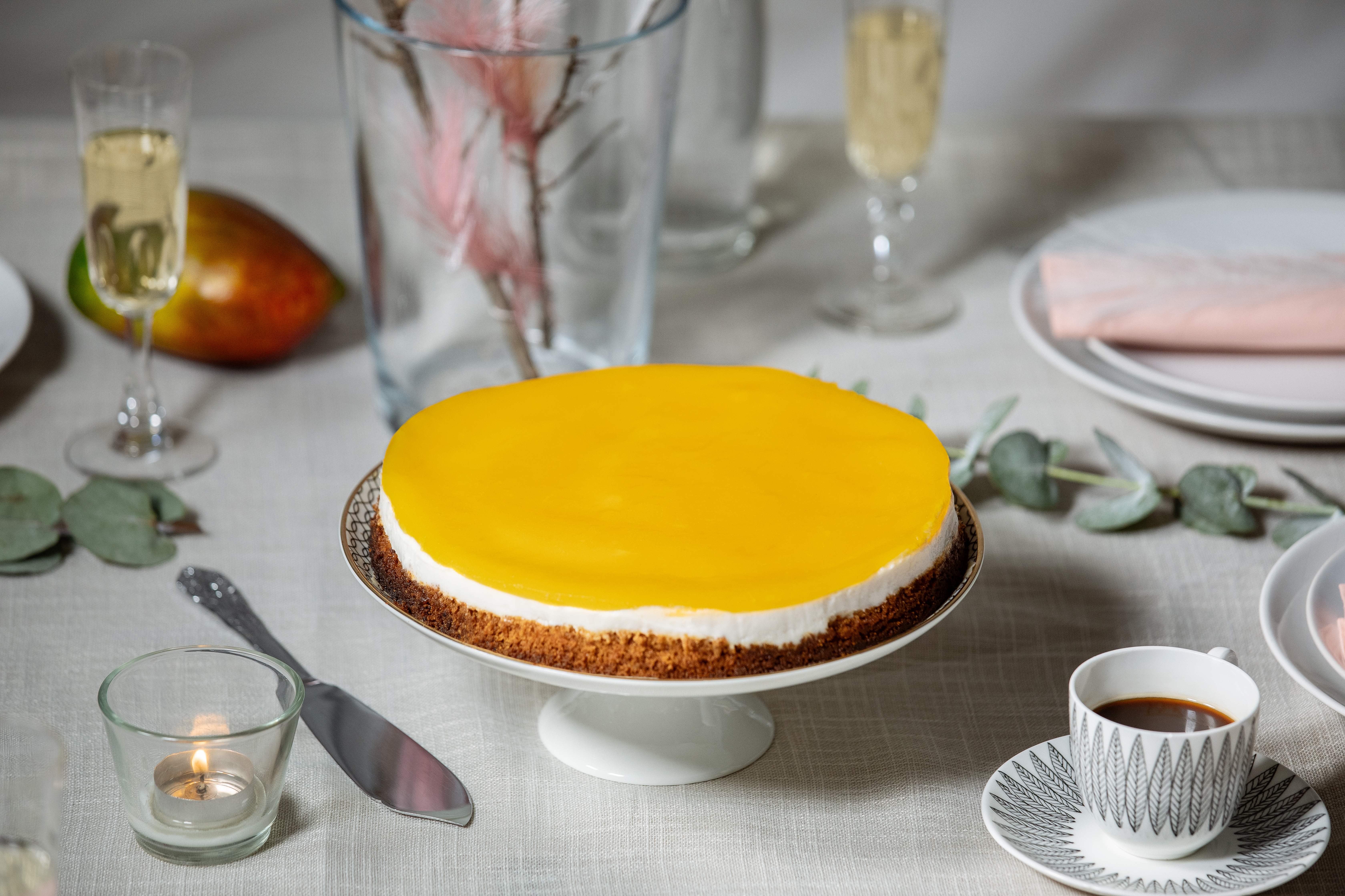 Vegansk cheesecake med mangoglasyr på ett tårtfat.
