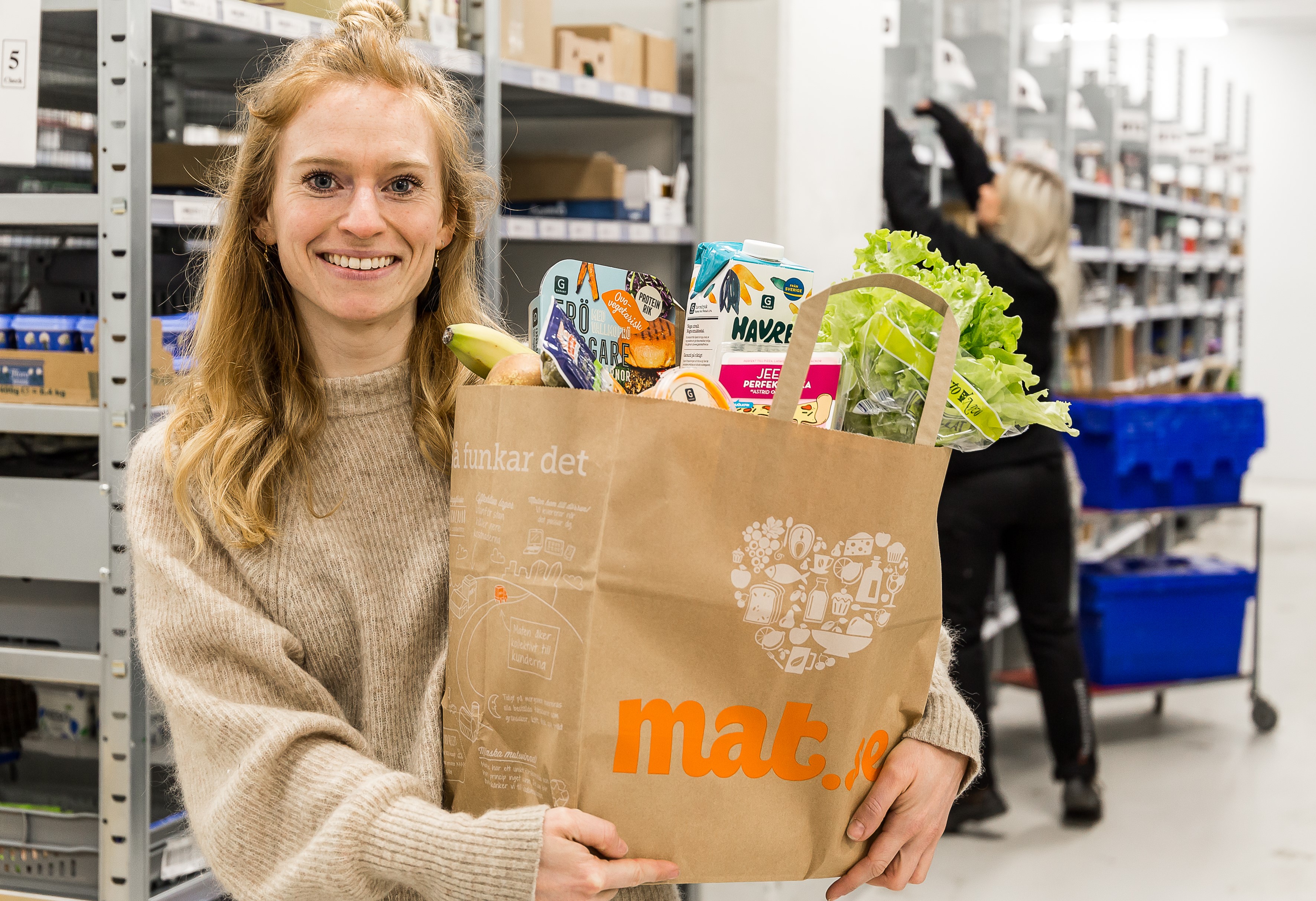 Person står i en lagerlokal med en matkasse fylld med veganska produkter