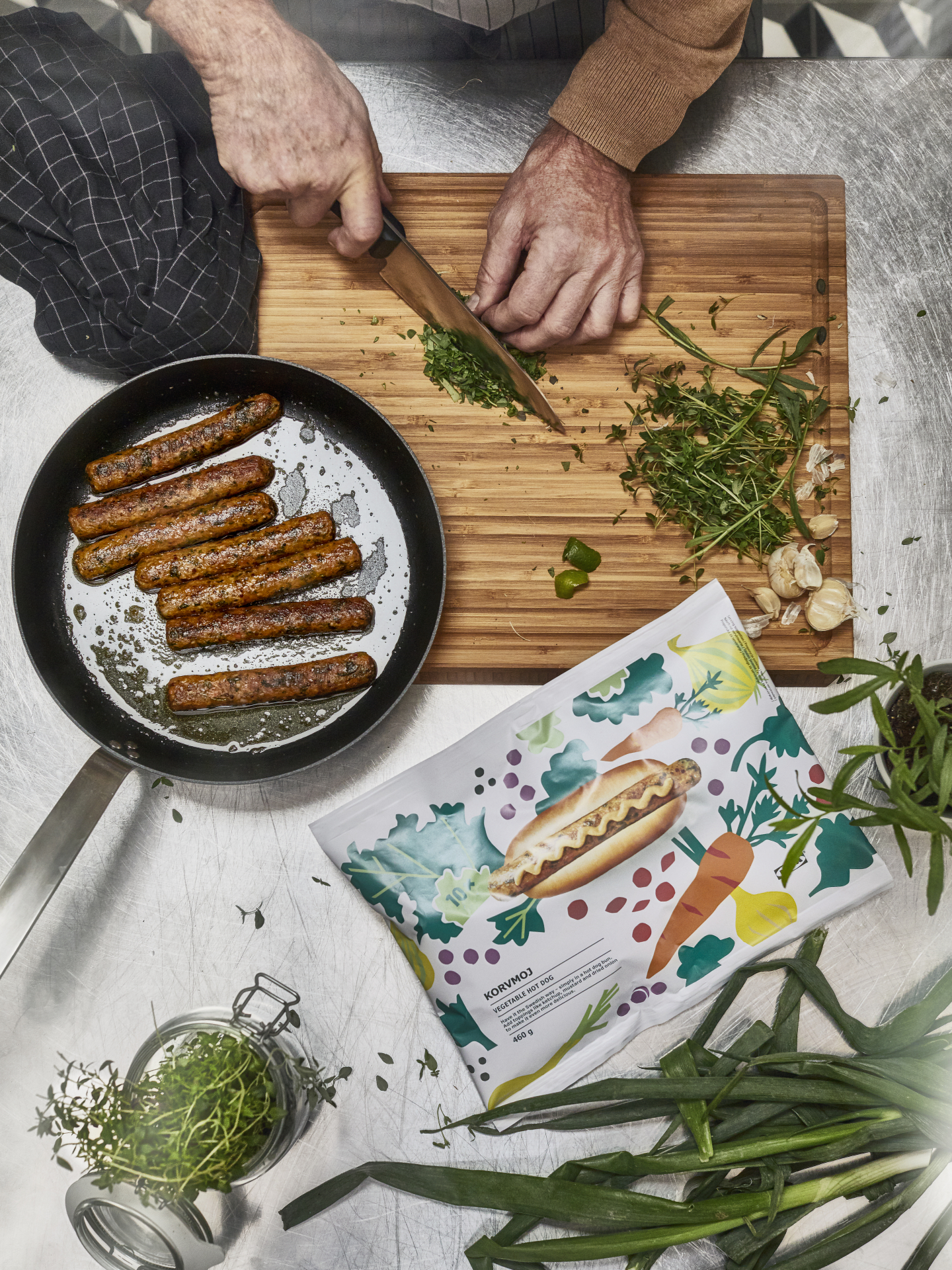 Händer hackar gräslök och det ligger ett par veganska korvar på en panna intill