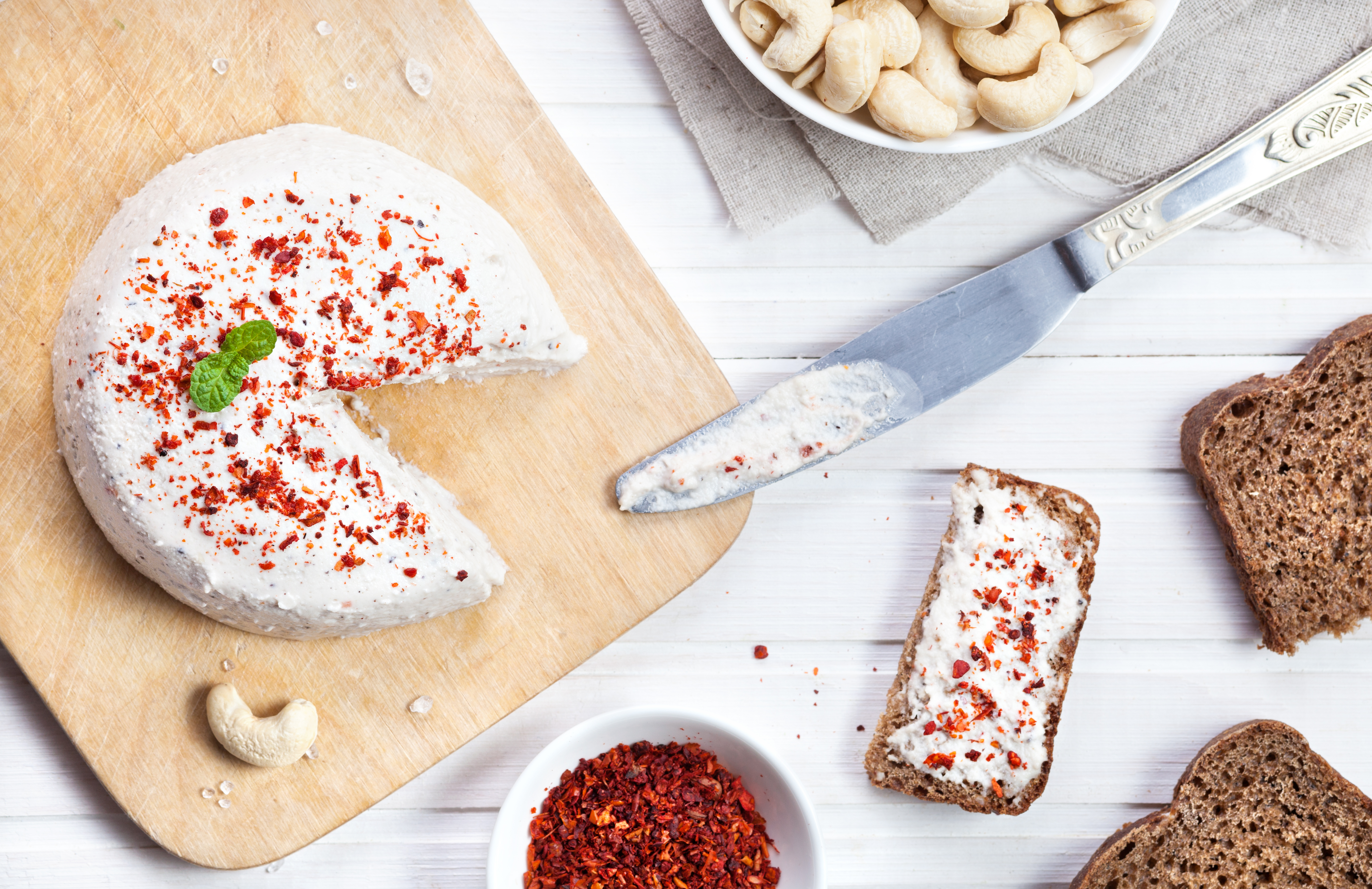 Vegansk cashewost toppad med chiliflingor på en skärbräda.