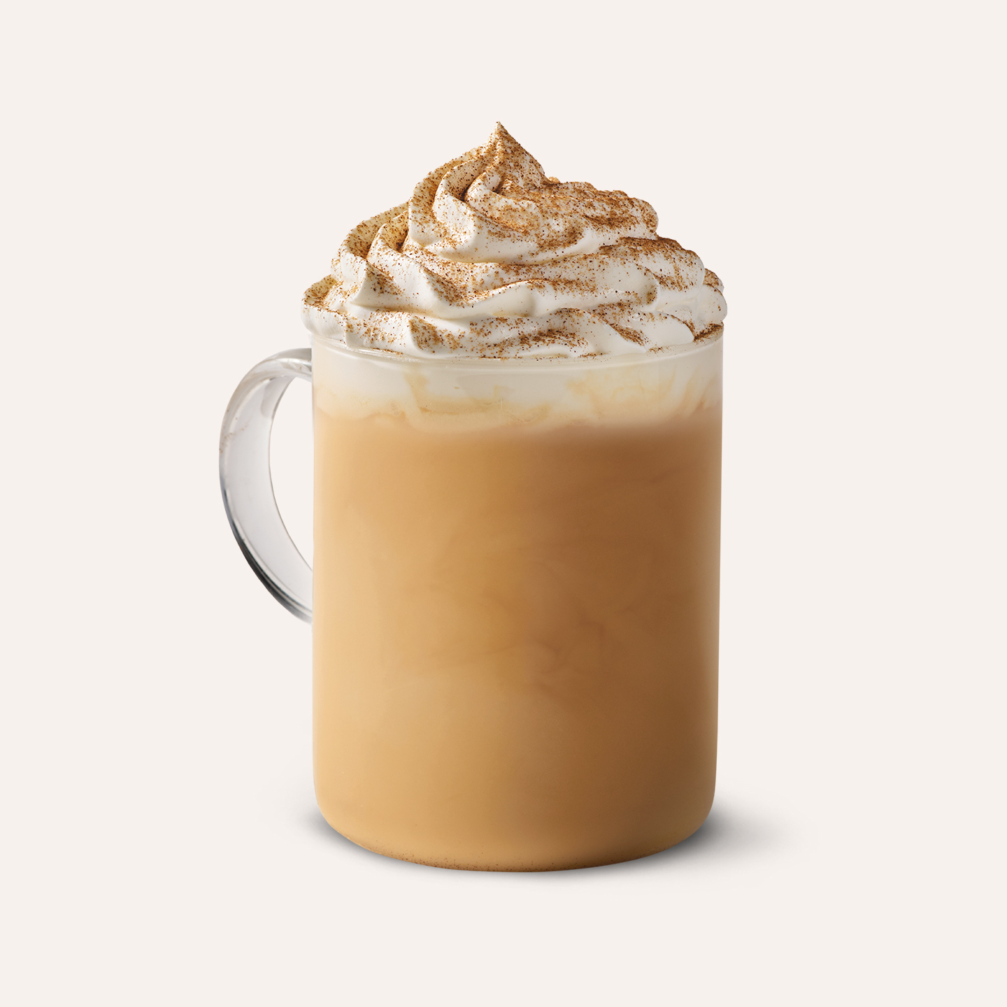 En glaskopp med pumpkin spice latte i och grädde toppad med kanel på toppen mot en vit bakgrund.