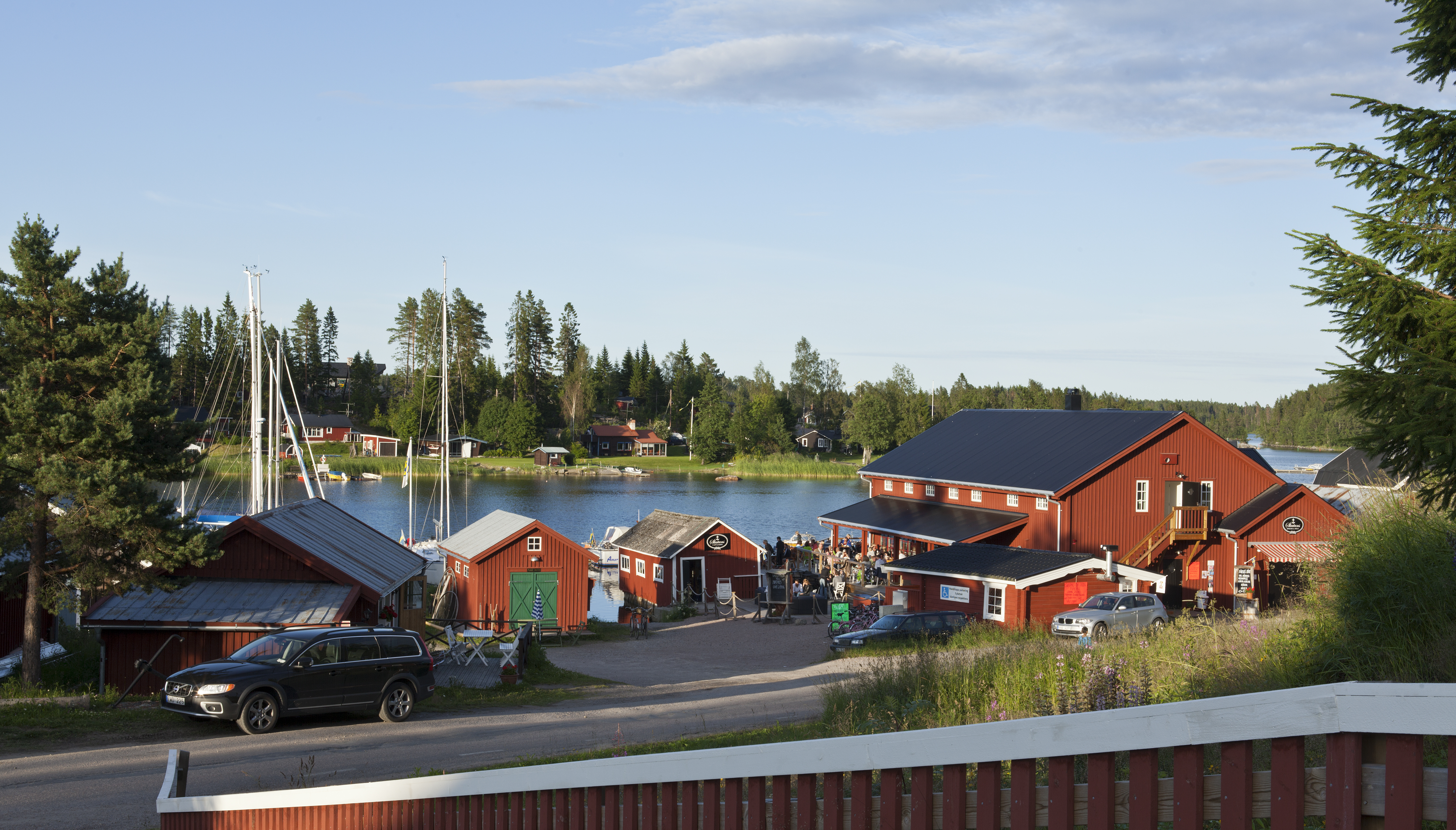 View of several red buildings in evening lit on July 17, 2012 in Jungfrukusten, Sweden. Gravel road, wooden fence, bridge and a Restaurant.