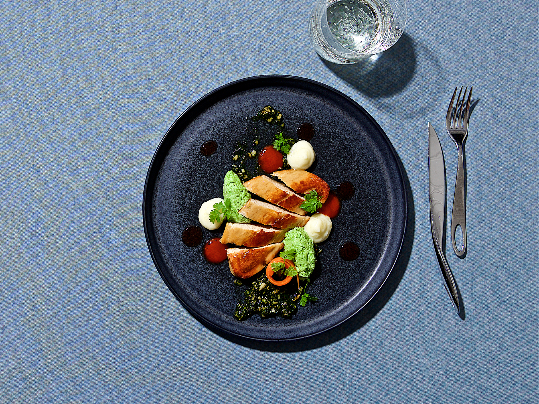 Vegansk quornfilé på tallrik med bestick och vattenglas runtom, fotat ovanifrån mot blå bakgrund.