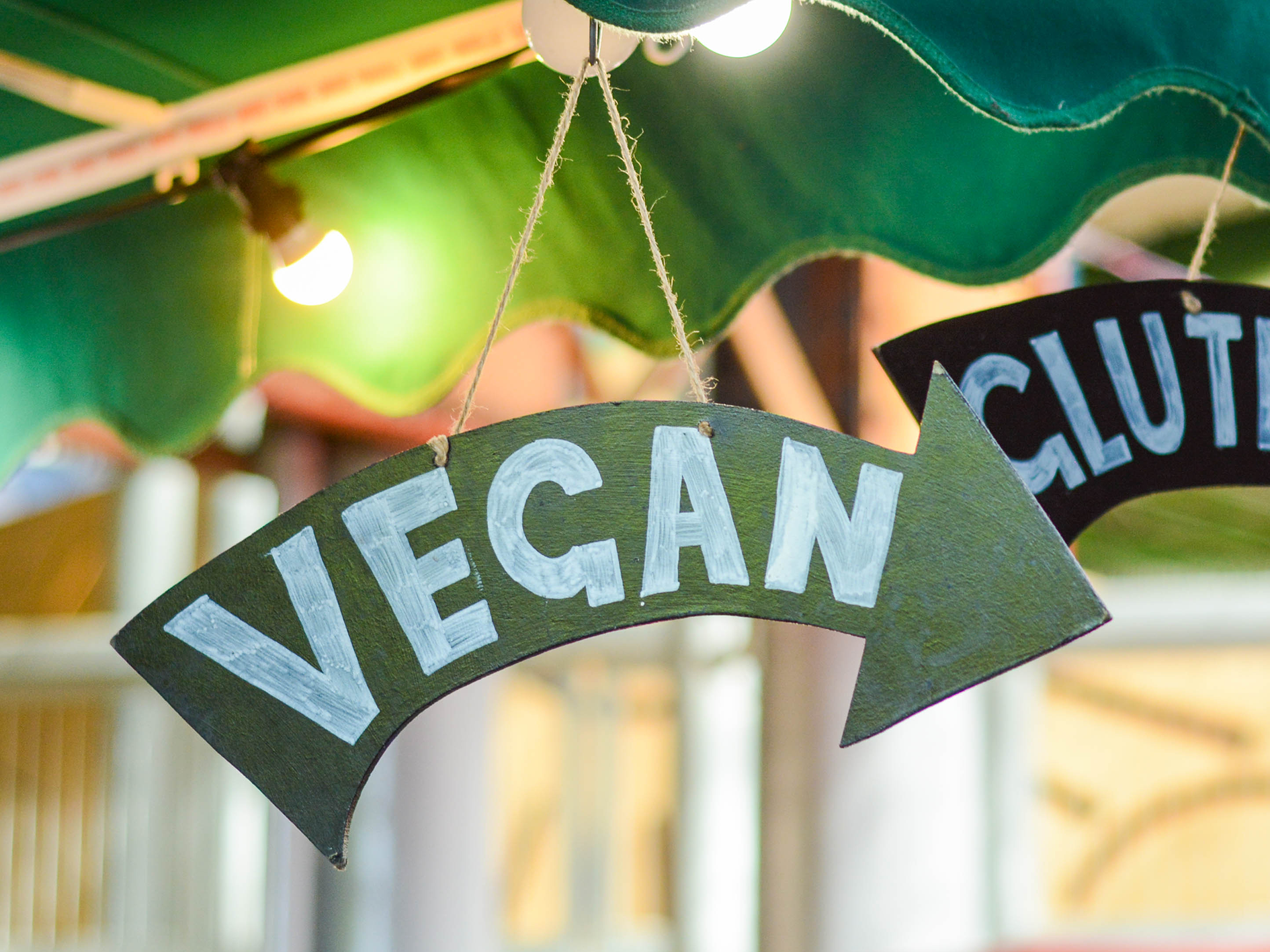Pilformad skylt med texten "vegan", hängandes från ett parasol i dovt upplyst miljö.