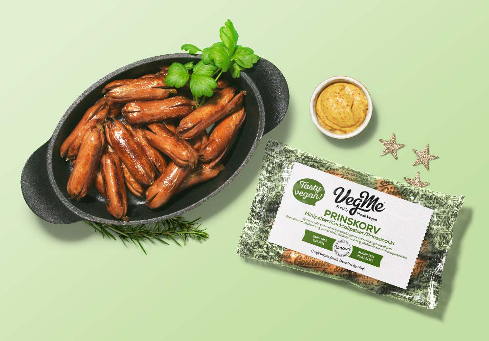 Prinskorv från VegMe i gjutjärnsgryta mot grönbakgrund, med förpackning och en liten skål senap bredvid.