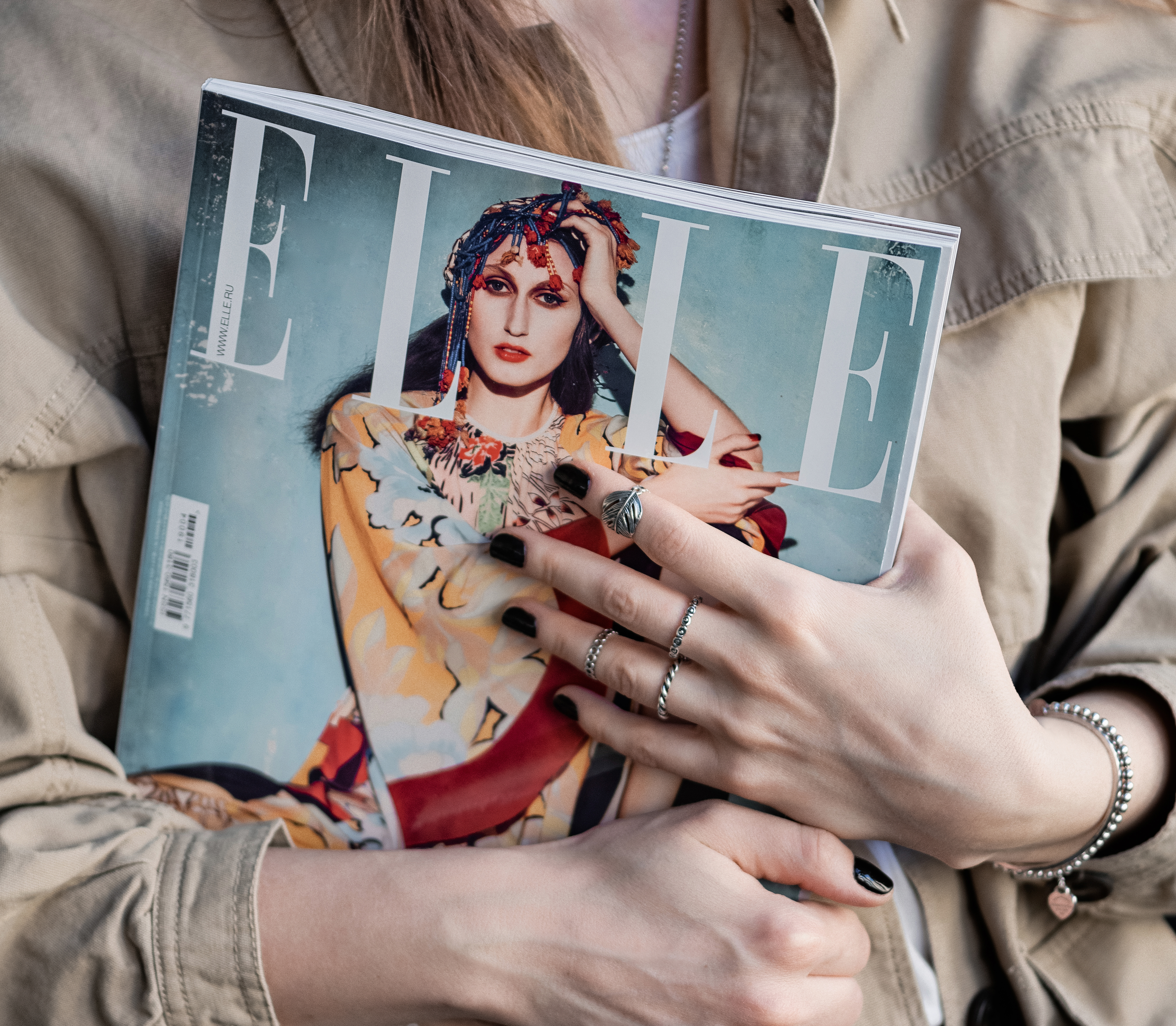 Person iklädd beige jacka håller i ett exemplar av ELLE magazine