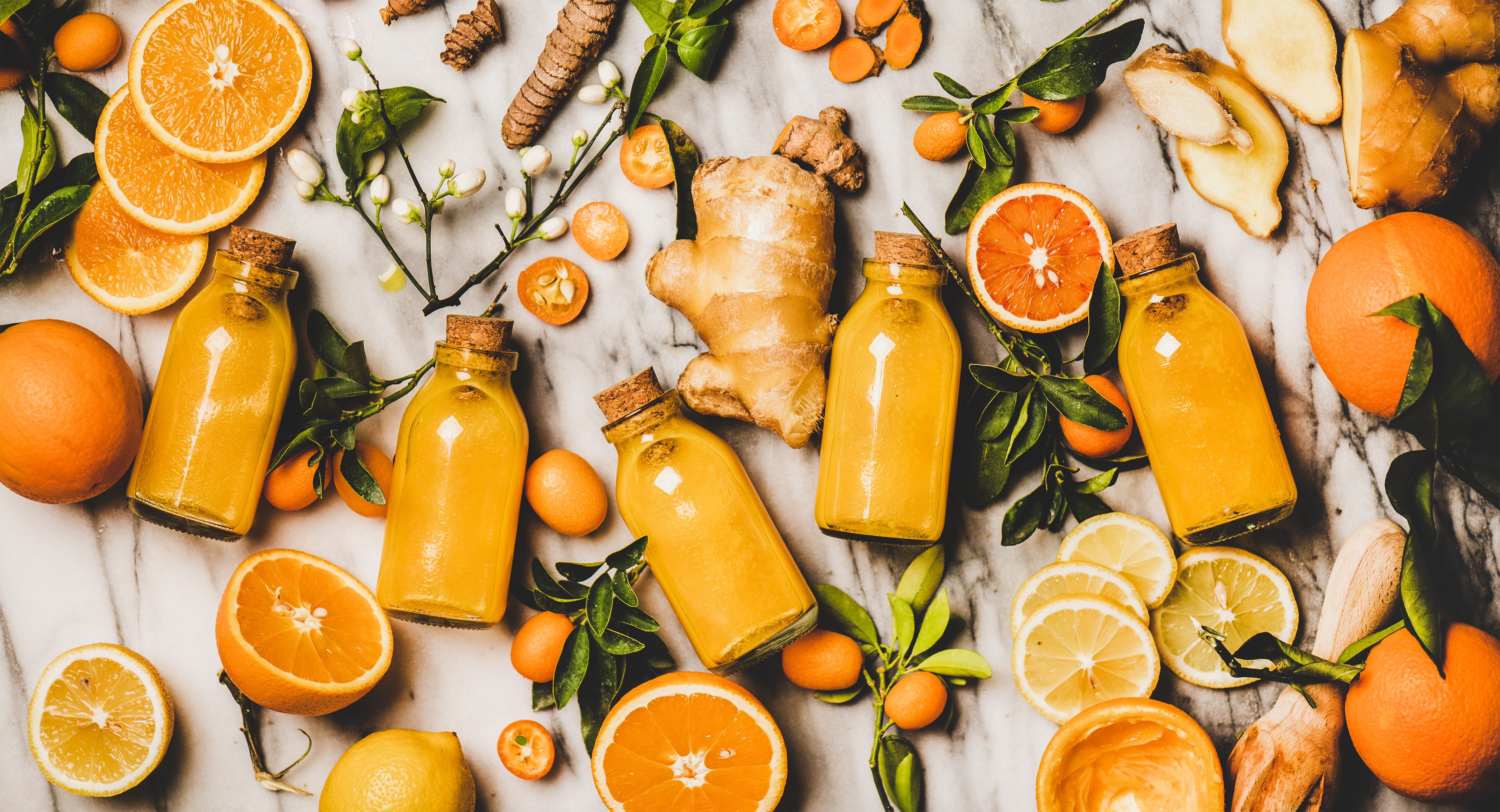 Apelsin, ingefära och små flaskor med apelsinjuice, utlagt över yta.