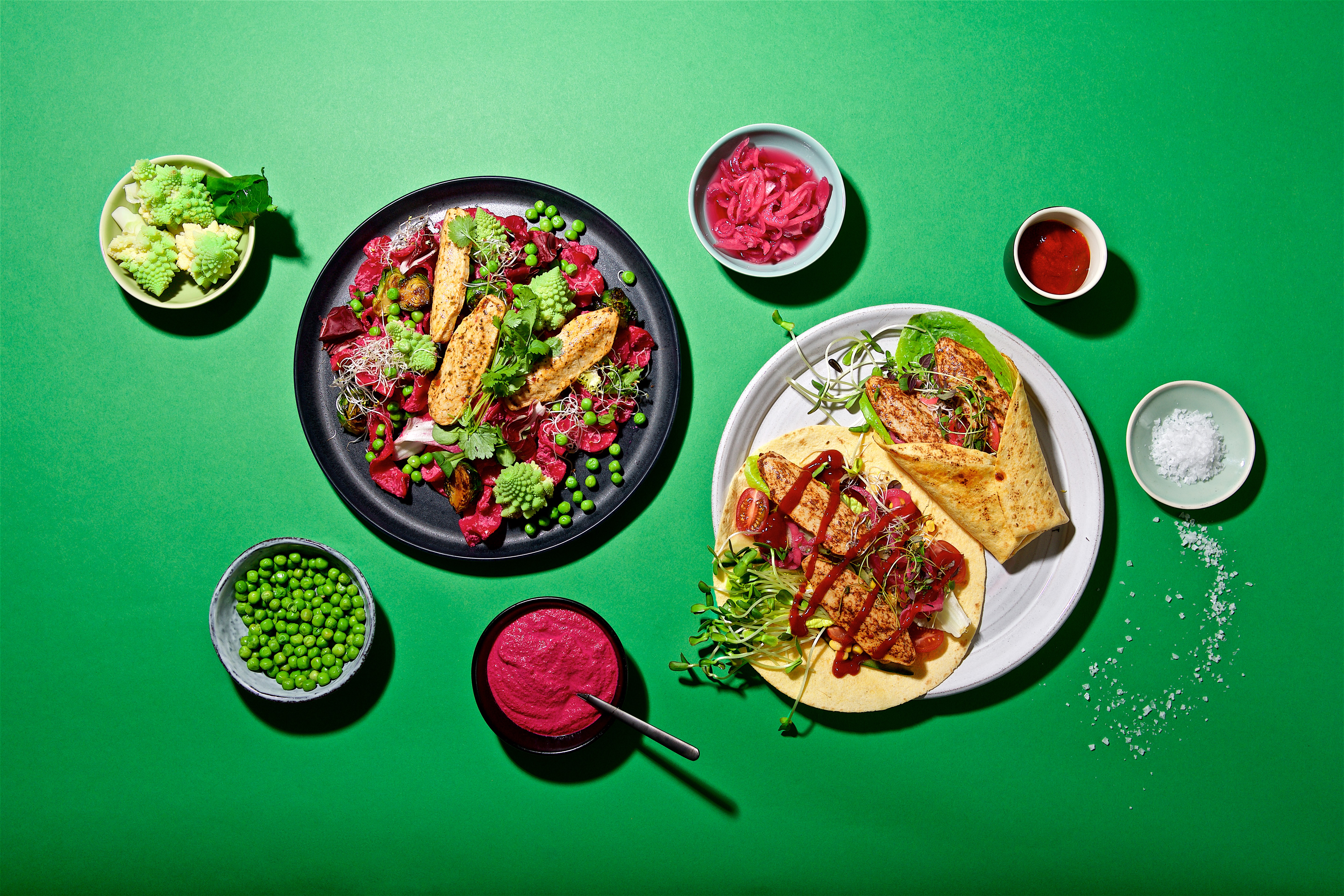 veganska filléer i en sallad på en tallrik och en i wrap på en annan tallrik uppdukat på ett grönt bord med tillbehör.