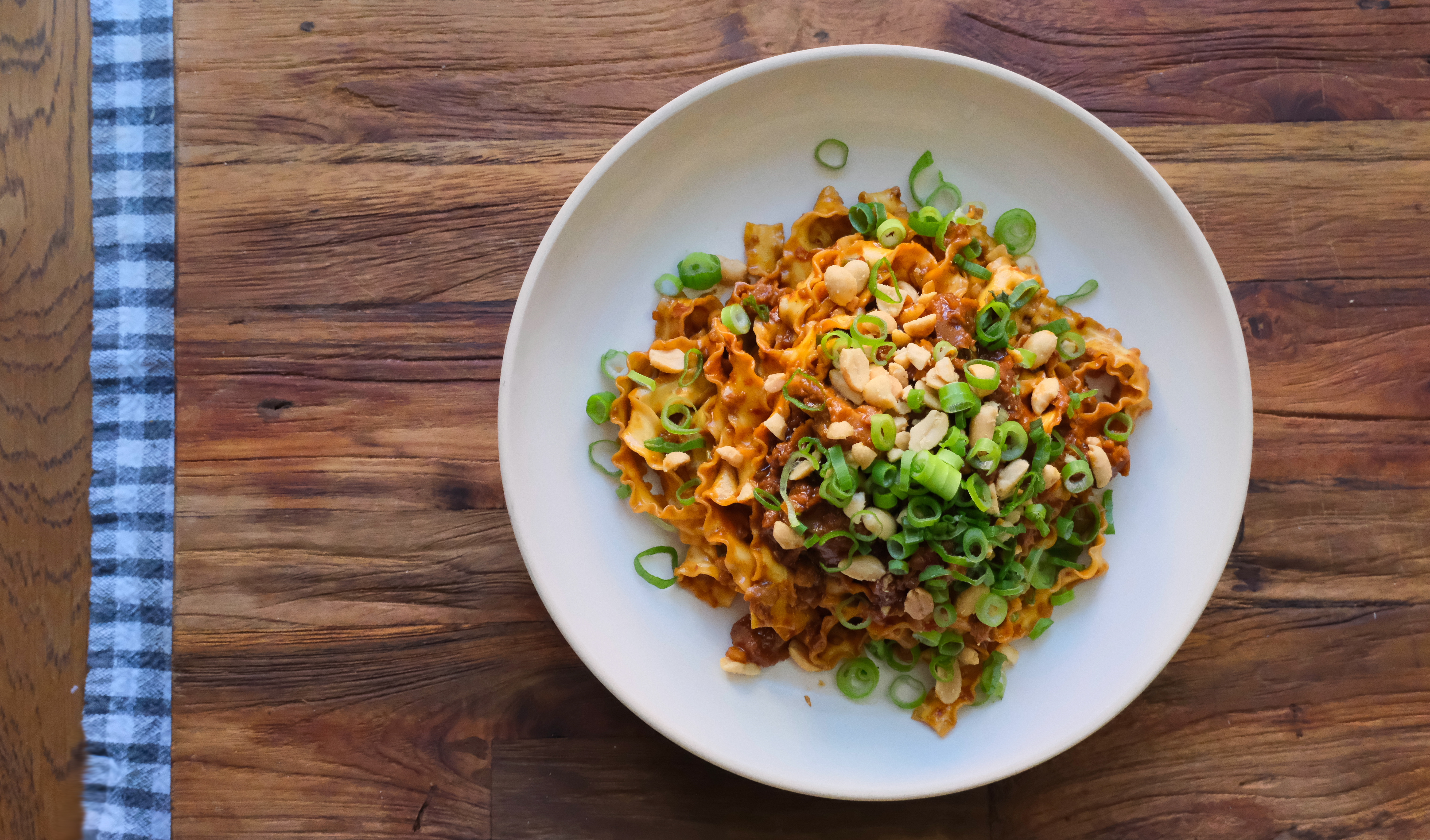 Veganska nudlar uppdukad på en vitt tallrik på ett träbord.