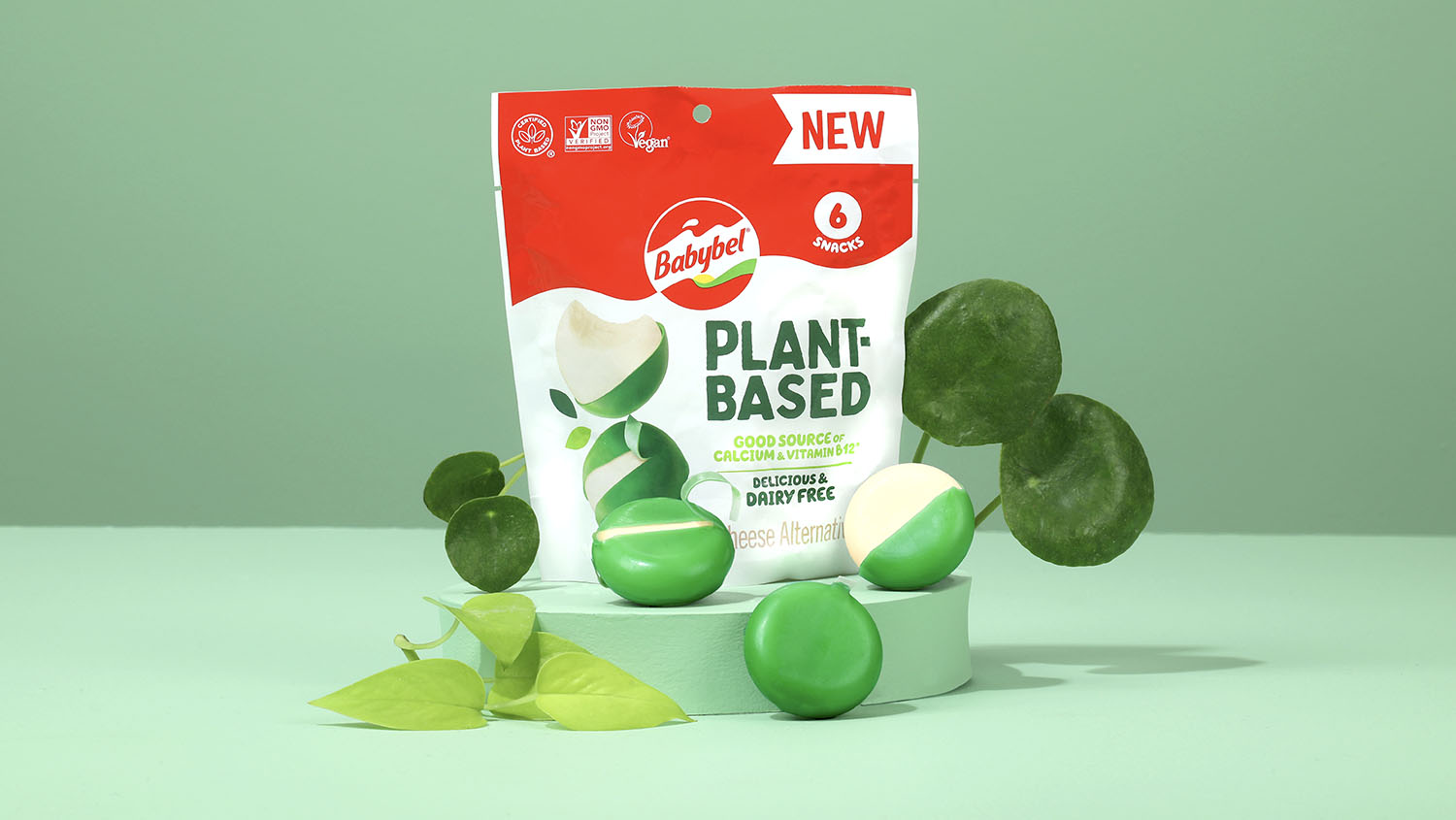Växtbaserade Babybel-ostar i grönt vax framför produktpåsen mot en grön bakgrund.