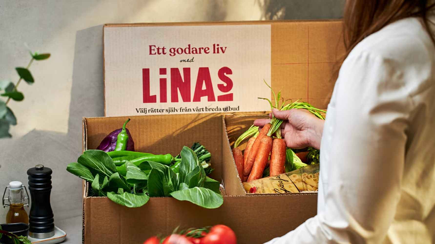 En kartong från Linas Matkasse med olika grönsaker och råvaror i.