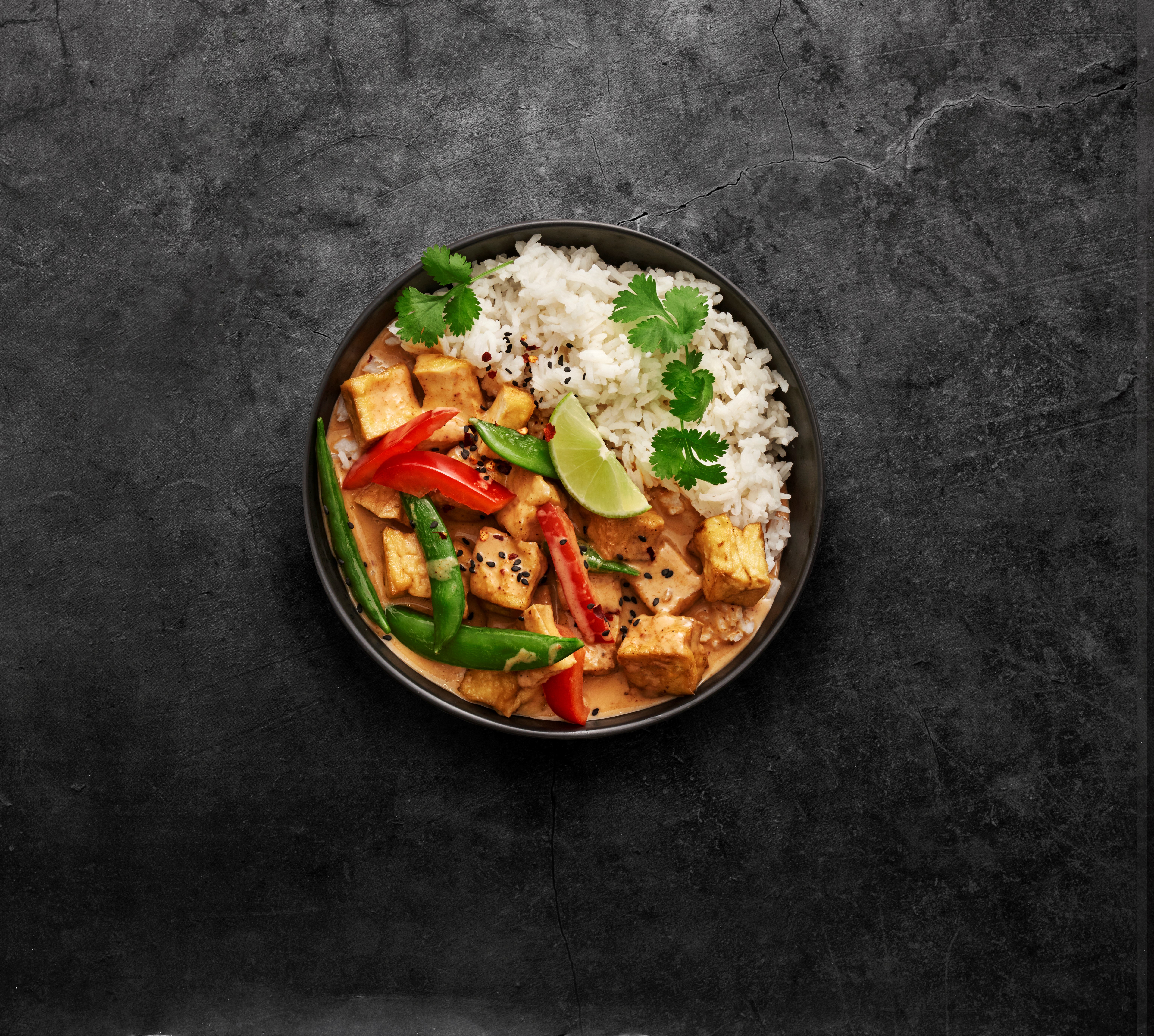 röd currygryta med ris i en djuptallrik vinkel uppifrån mot en granitgrå bakgrund
