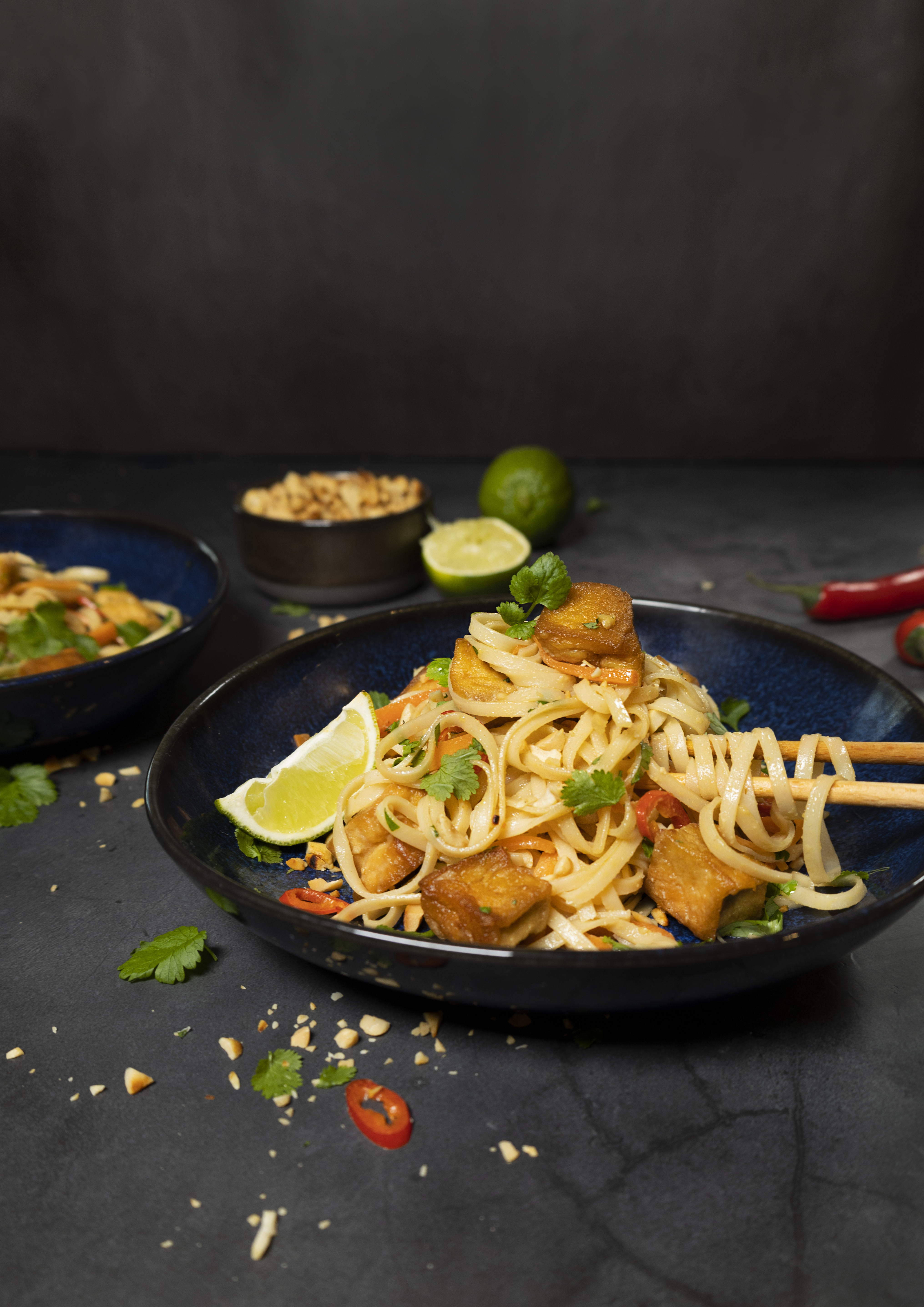 Veganska pad thai med tofu i en mörkblå djuptallrik mot en mörkgrå bakgrund.
