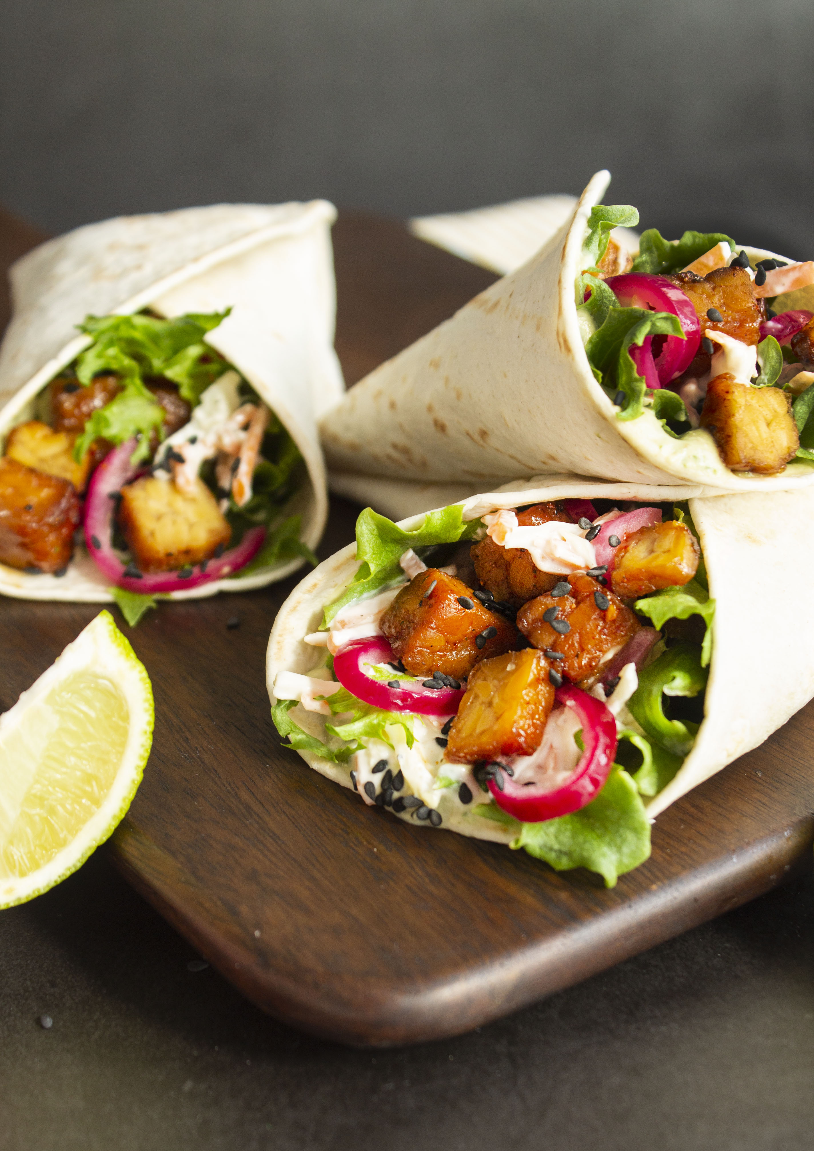 tre veganska wraps uppstaplade på en skärbräda i trä