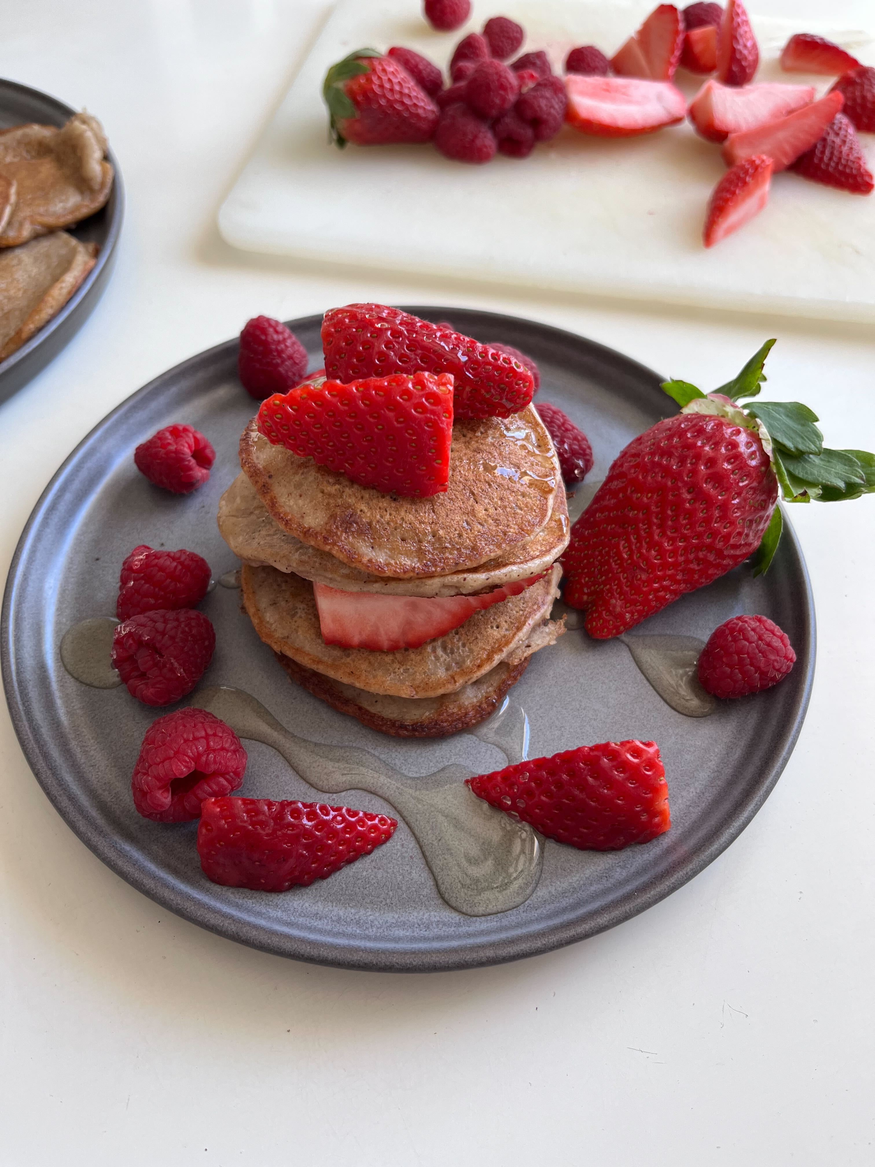 Amerikanska pannkakor staplade på ett grått fat med jordgubbar och hallon