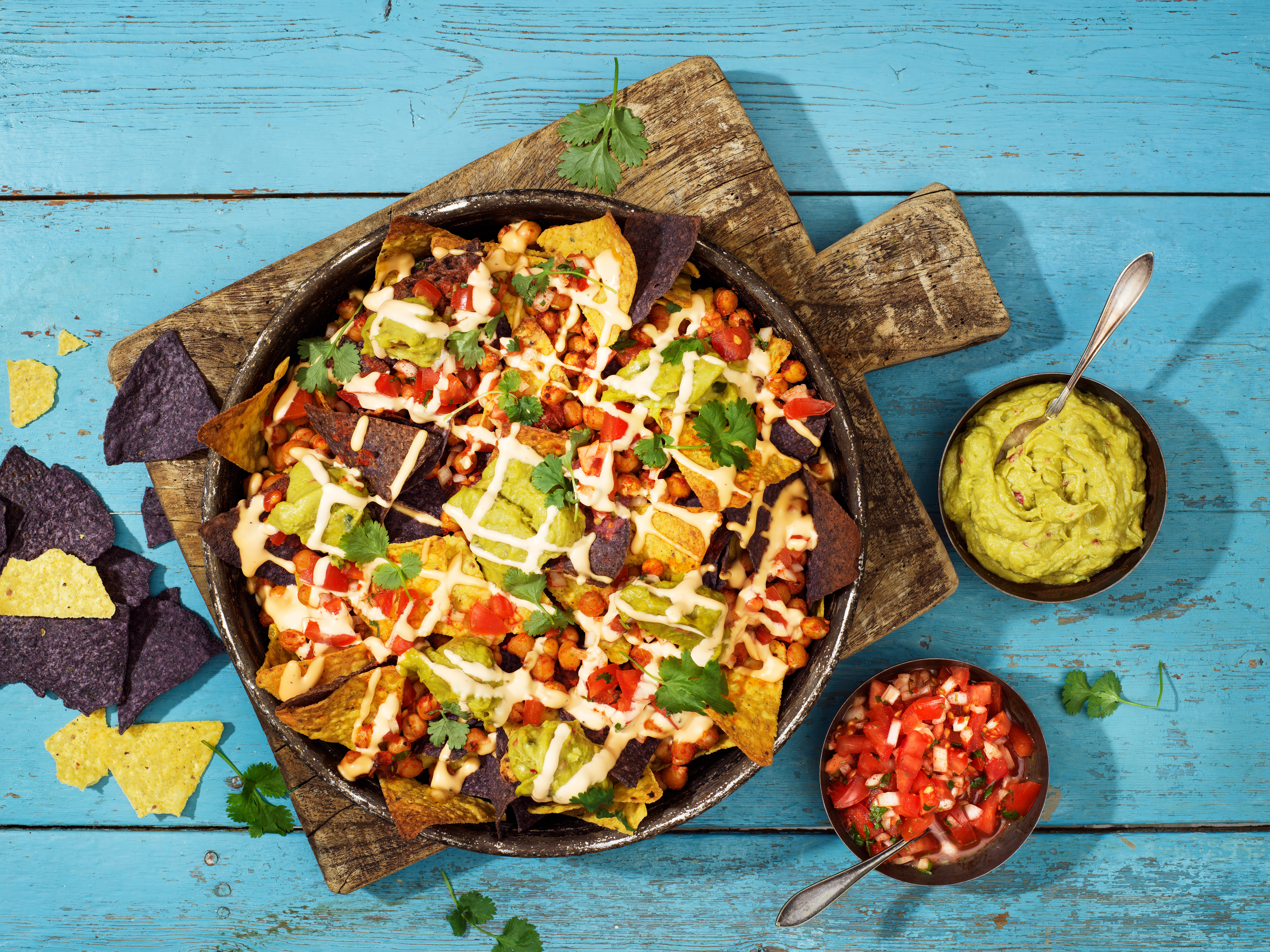 En tallrik med nachos på en skärbräda i trä som står på ett turkost träbord