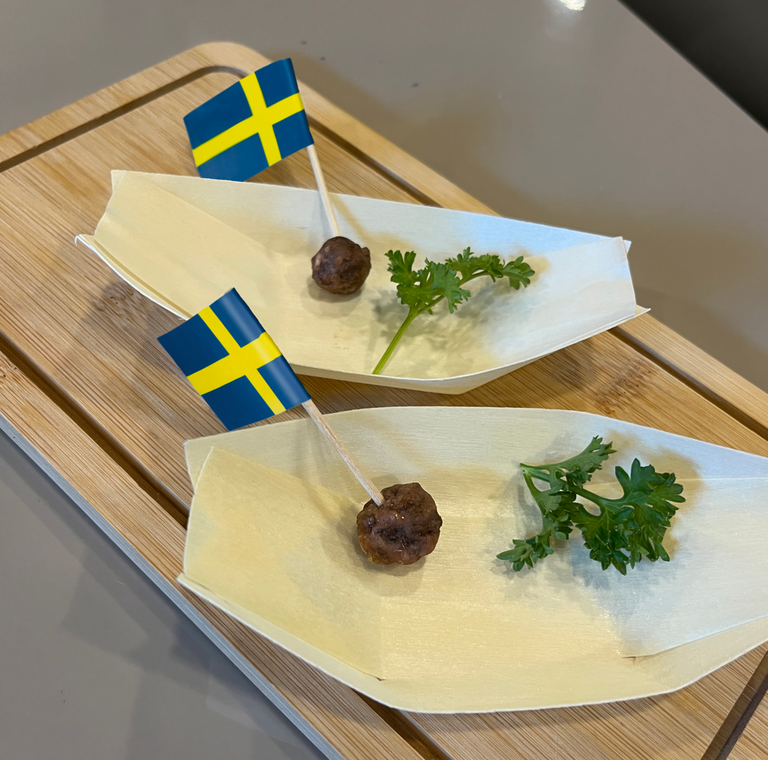 Två odlade köttbullar på vita fat med små svenska flaggor i och kvistar med persilja på sidan om