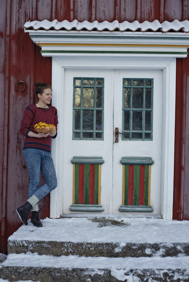 Kvinna som står lutan mot en röd vägg på ett hus