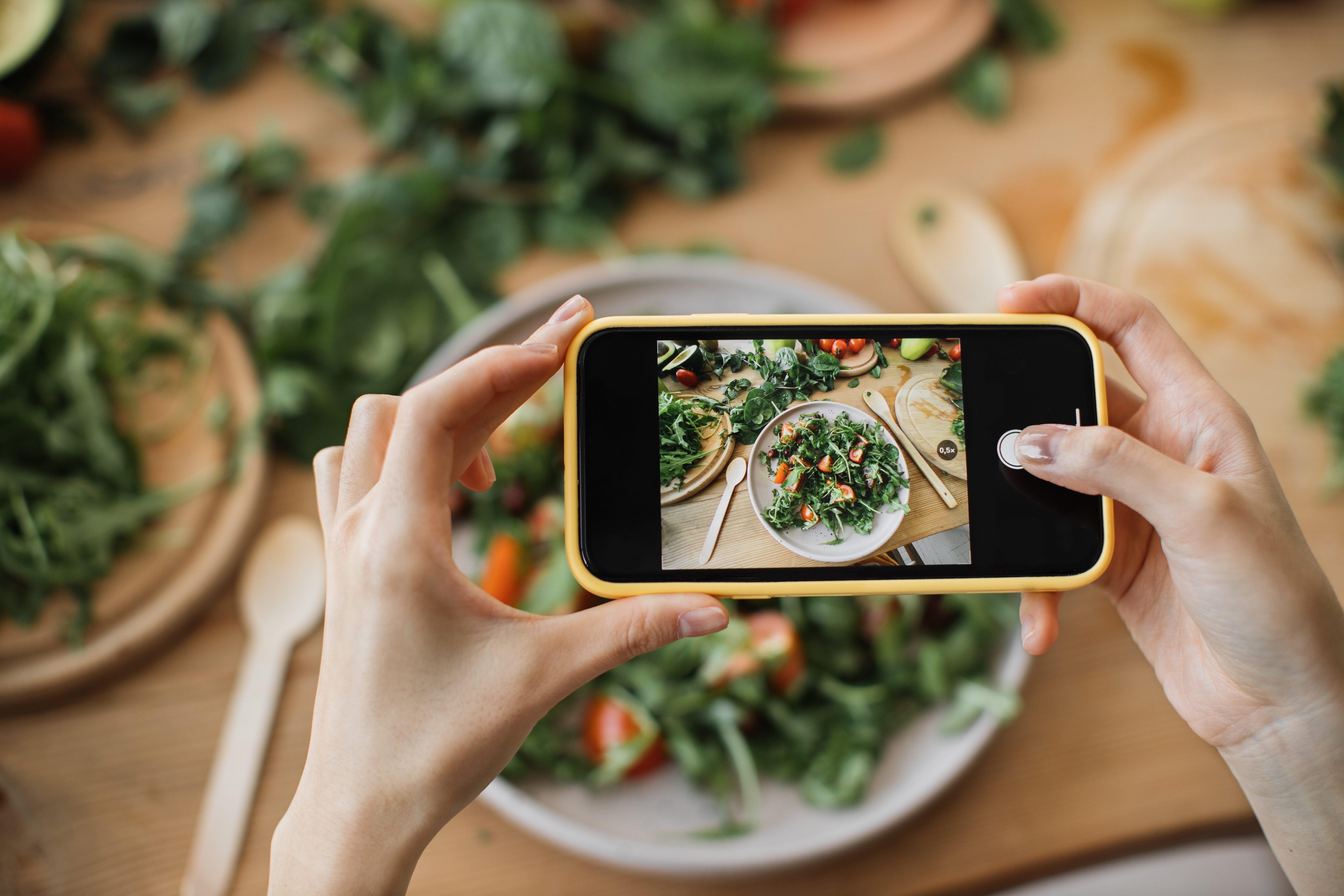 Kvinnahänder tar telefonfoto av matlunch eller middag. Grönsakssallad, avokado, ruccolatomater. Smartphonefotografering för sociala nätverk. Vegetarisk hälsosam mat.