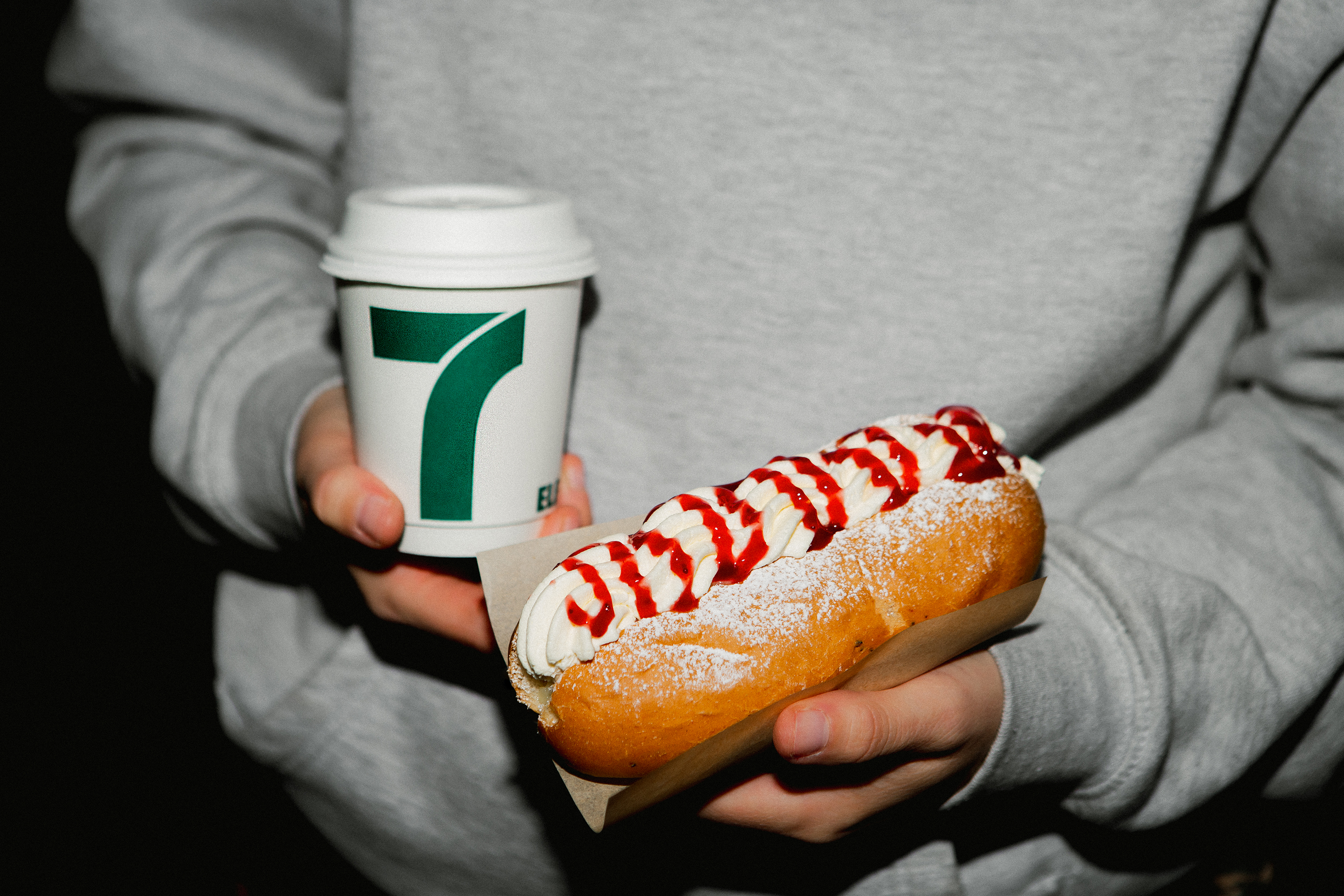 Man som håller en pappmugg med kaffe i andra handen och en semmelbakelse i korvbröd i den andra