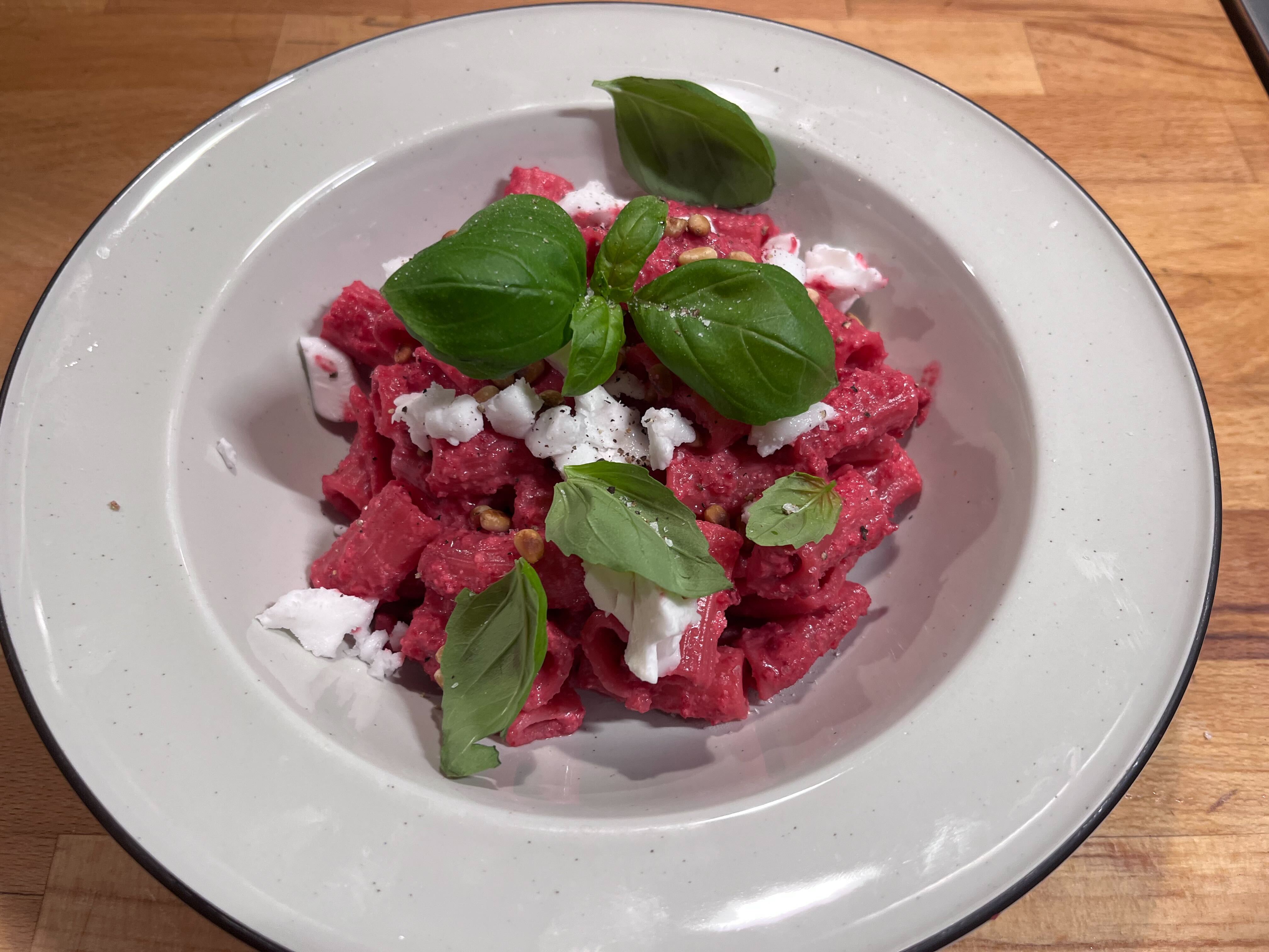 En djuptallrik med rödbetspasta, dekorerad med vegansk feta, pinjenötter och basilika