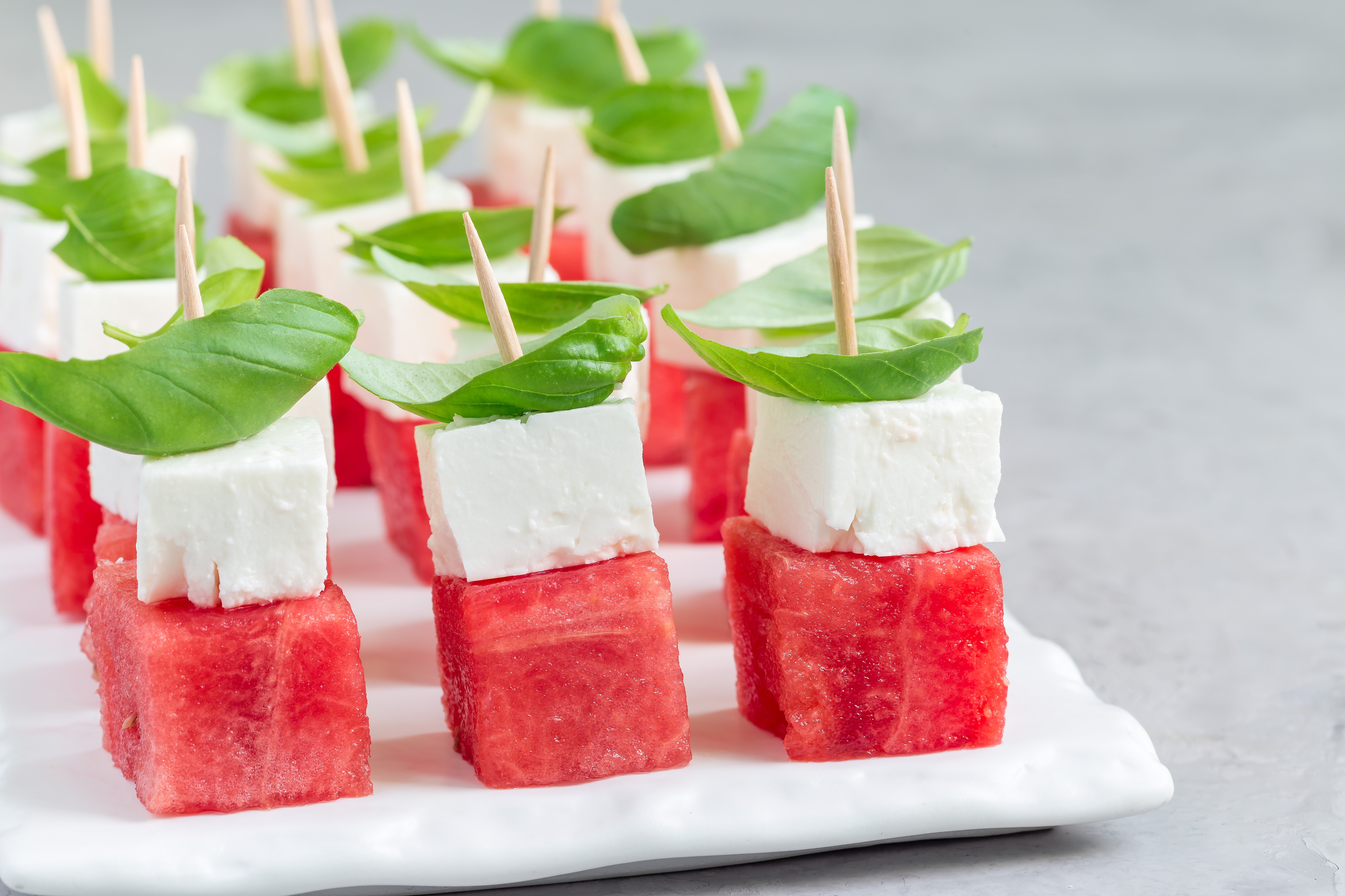 Snittar med melon, vegansk fetaost och basilika på ett vitt fat.