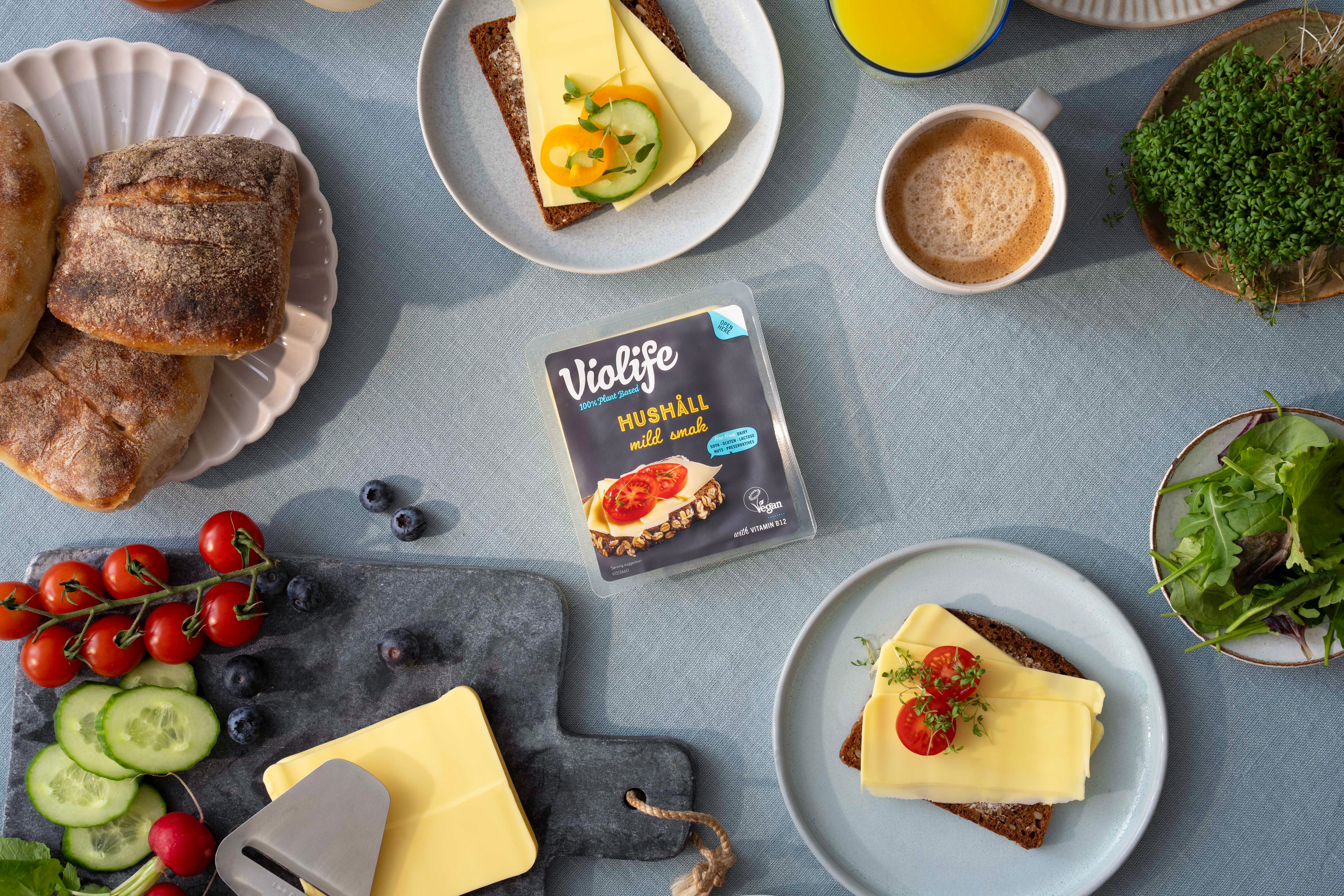ett frukostbord med bröd, tomater, gurka, grönt och växtbaserad ost