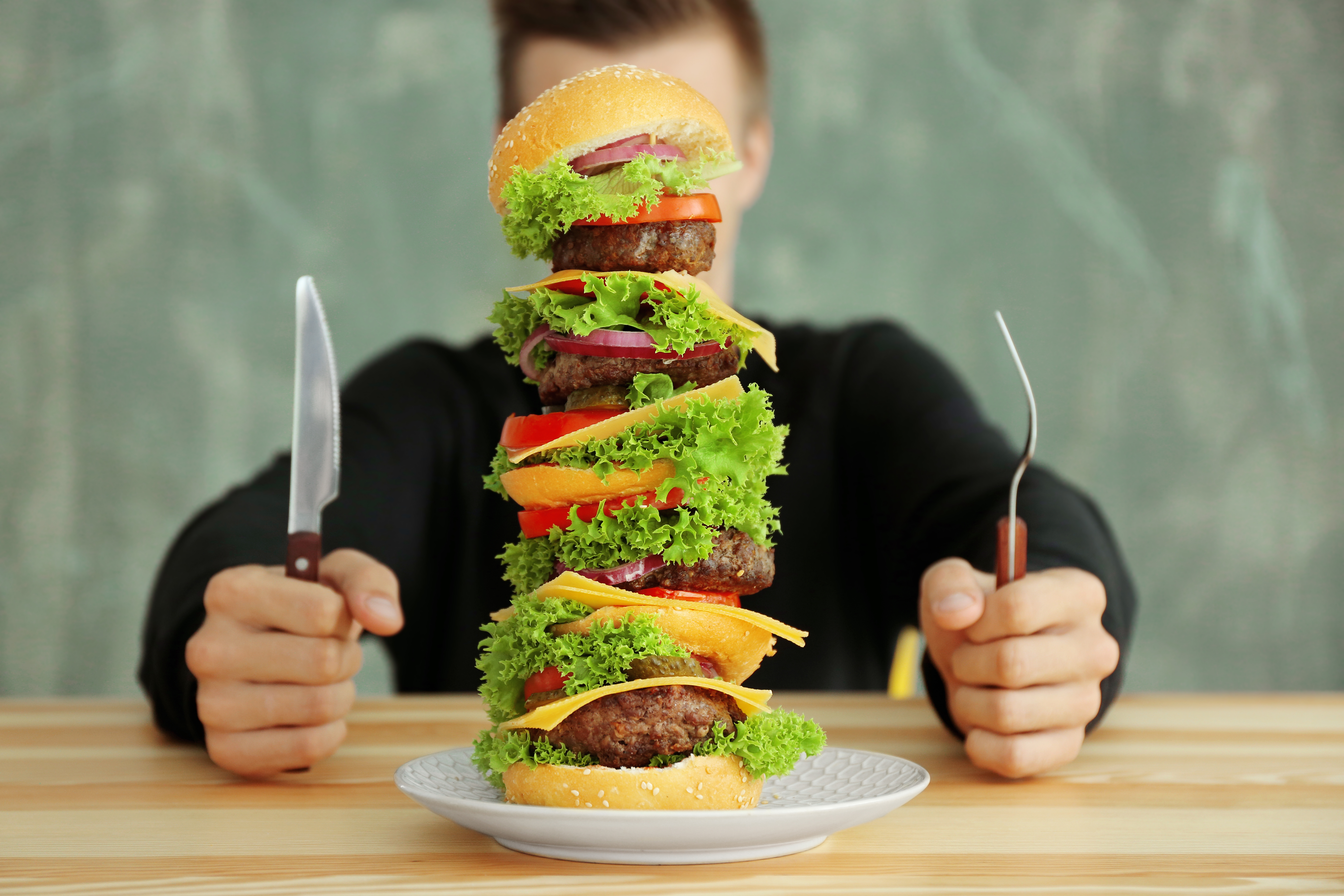 Man äter en stor hamburgare vid ett bord