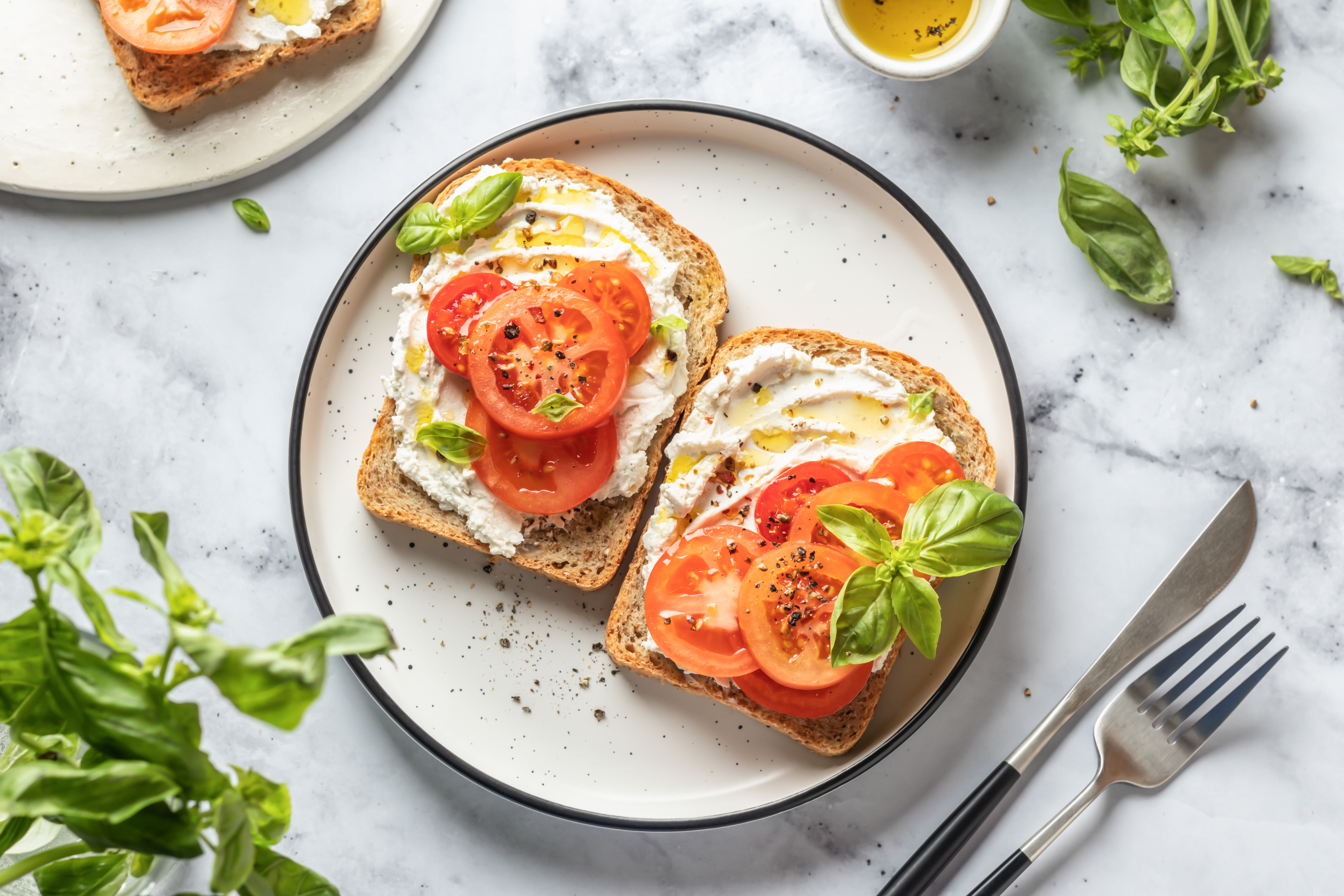 En tallrik med två smörgåsar med vegansk cream cheese och tomater, toppade med basilika