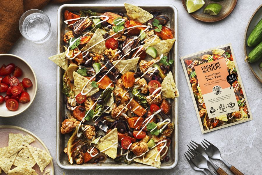 En plåt med dressade nachos på ett ljust bord med tillbehör på sidorna