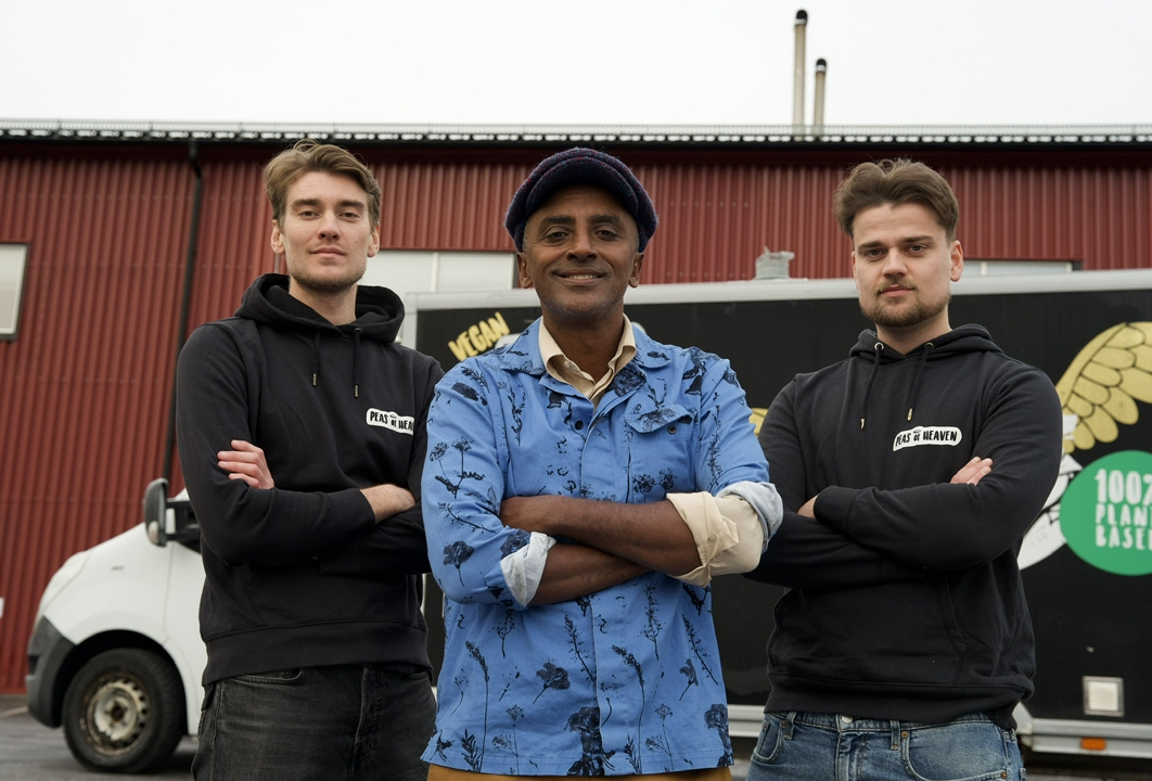 Tre män som står uppradade mot en röd vägg
