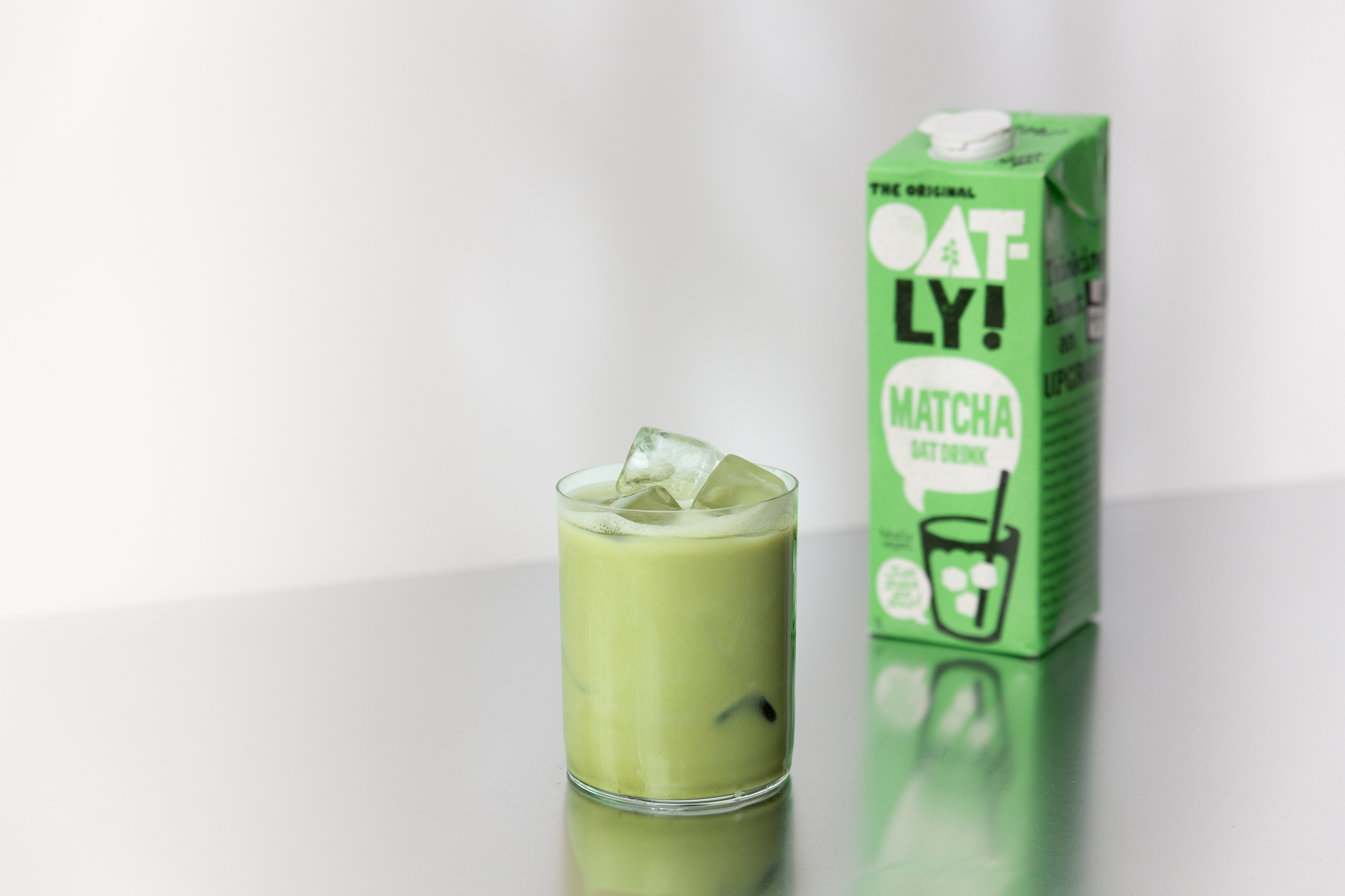 Ett glas med matcha latte och en tetra med färdigblandad matcha latte bredvid på ett silverbord.