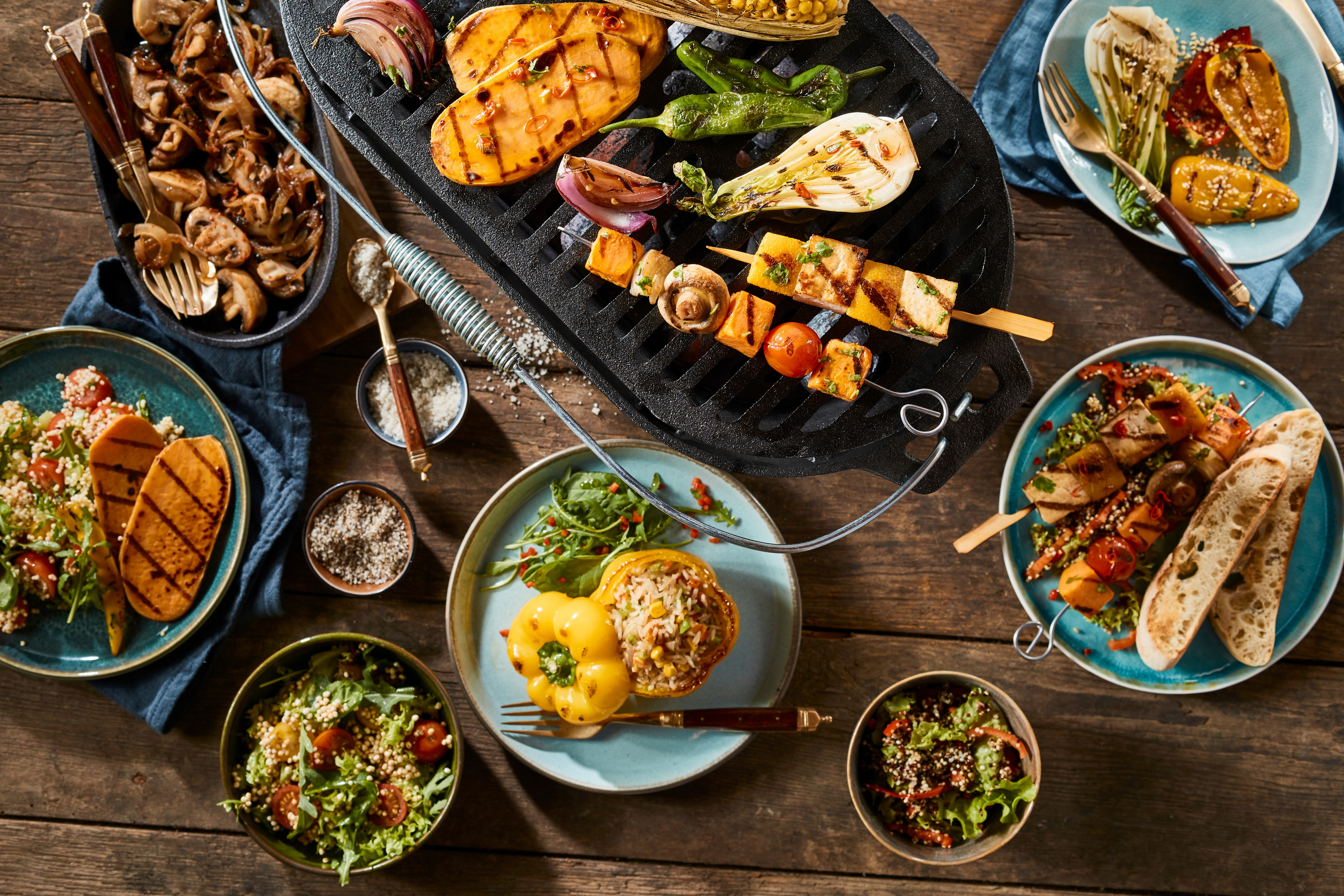 A vegetarian barbecue grill and various gourmet dishes on a rustic timber table.