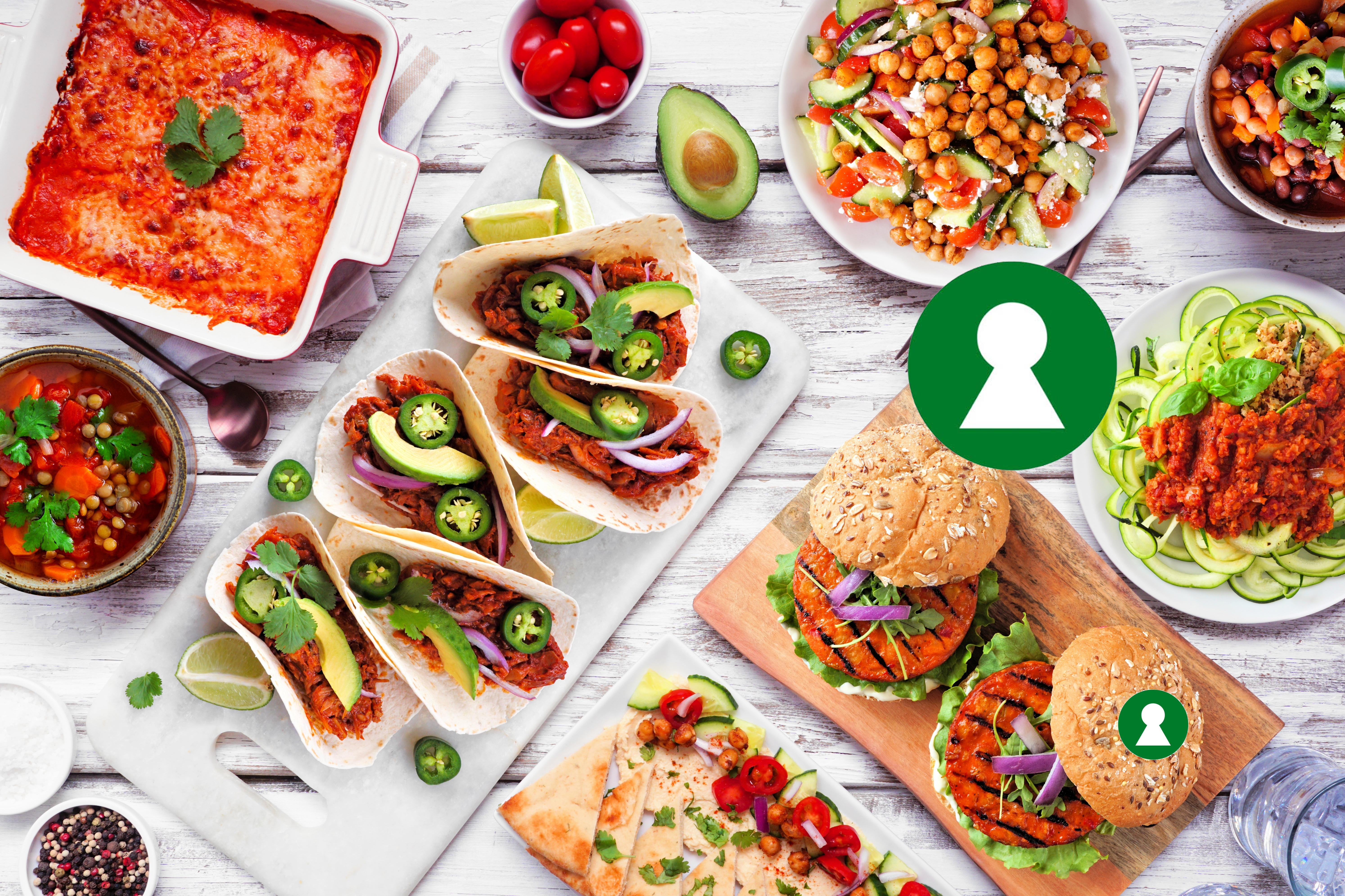 Healthy plant based vegetarian meal table scene. Above view on a white wood background. Jackfruit tacos, zucchini lasagna, walnut bolognese zoodles, chickpea burgers, hummus, soups, salad.