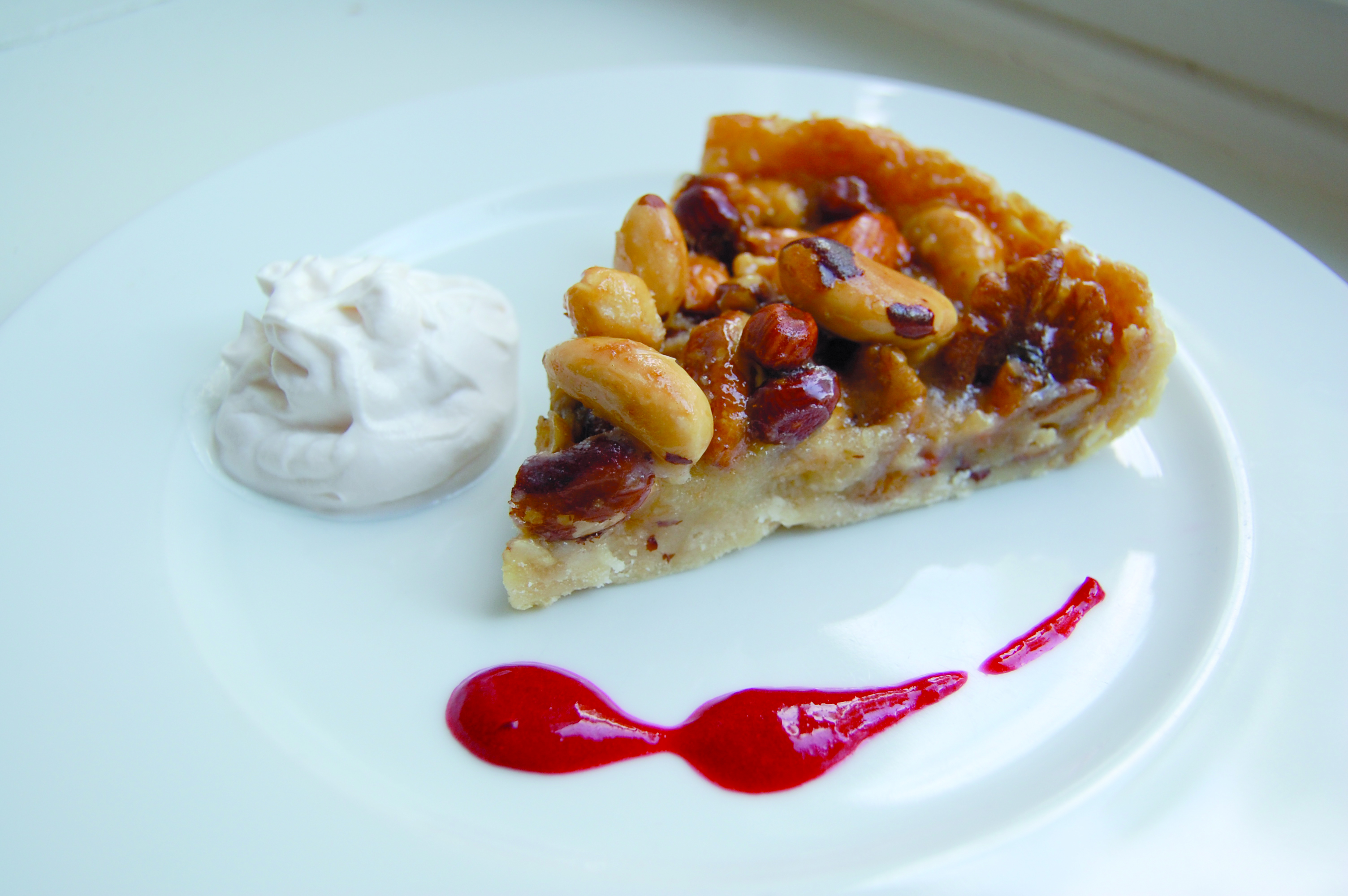 Vegansk nötpaj med vaniljgrädde och hallonsås på en vit tallrik