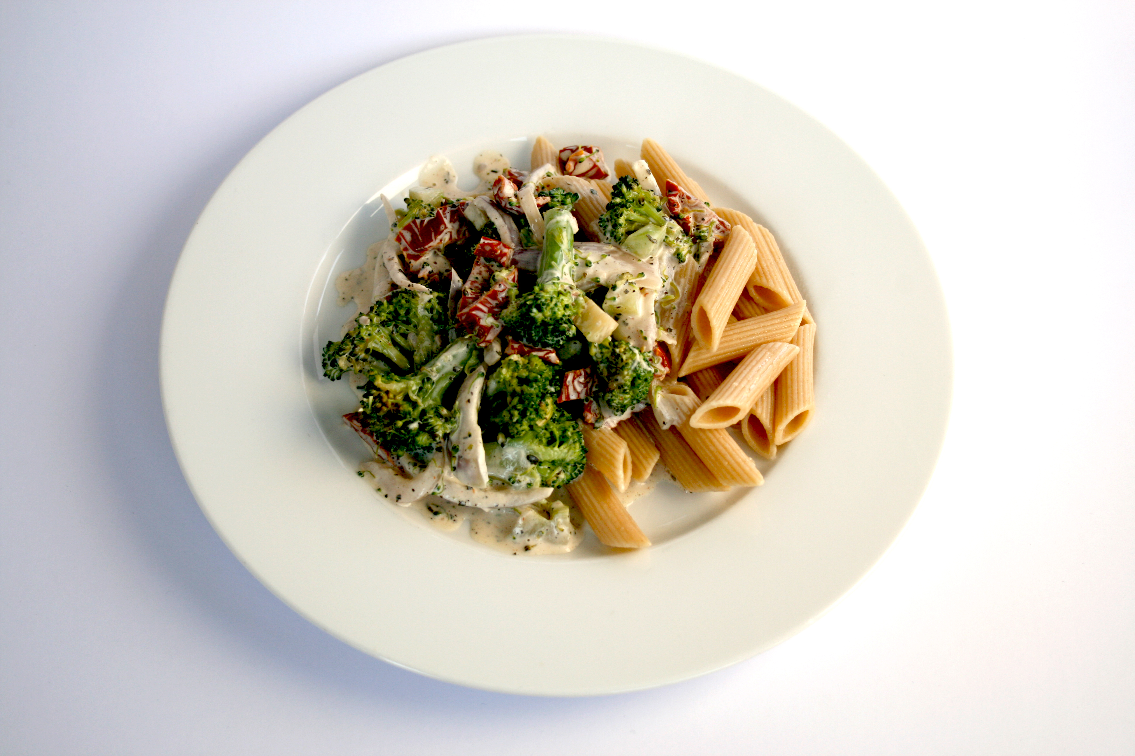 Pasta med broccoli och soltorkade tomater på en vit tallrik