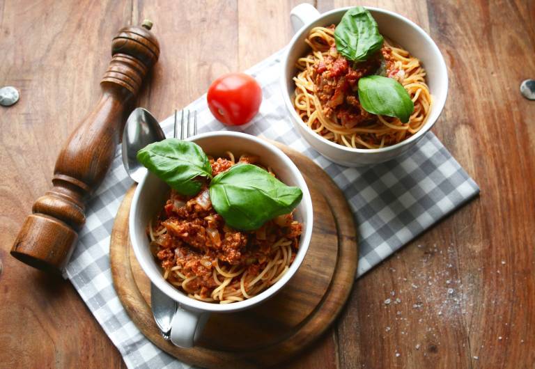 Två skålar med vegansk bolognese och pasta, garnerade med färsk spenat.